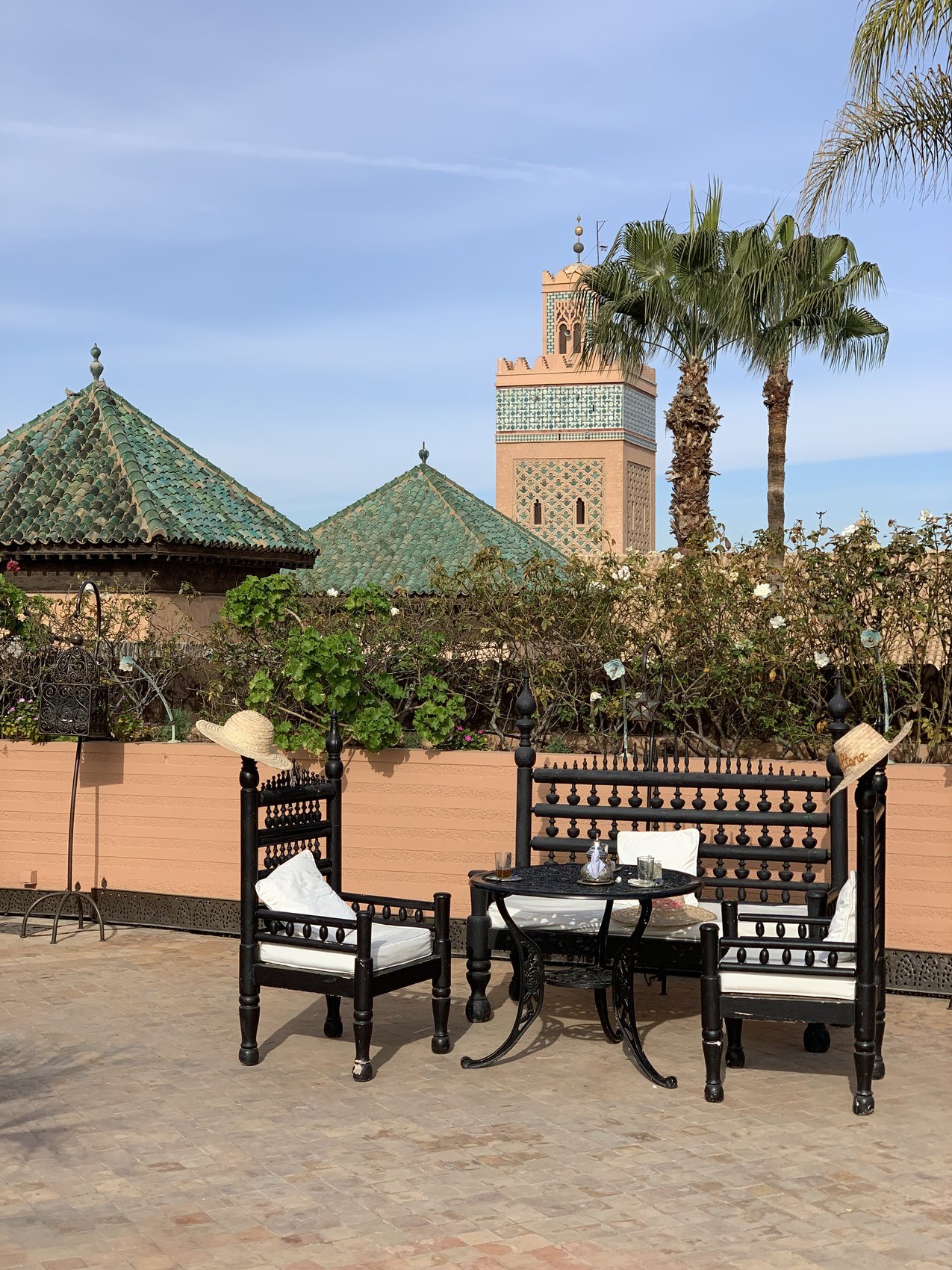 Carved black seating and a table on the terrace at La Sultana with the green tiled roofs and the Koutoubia minaret behind