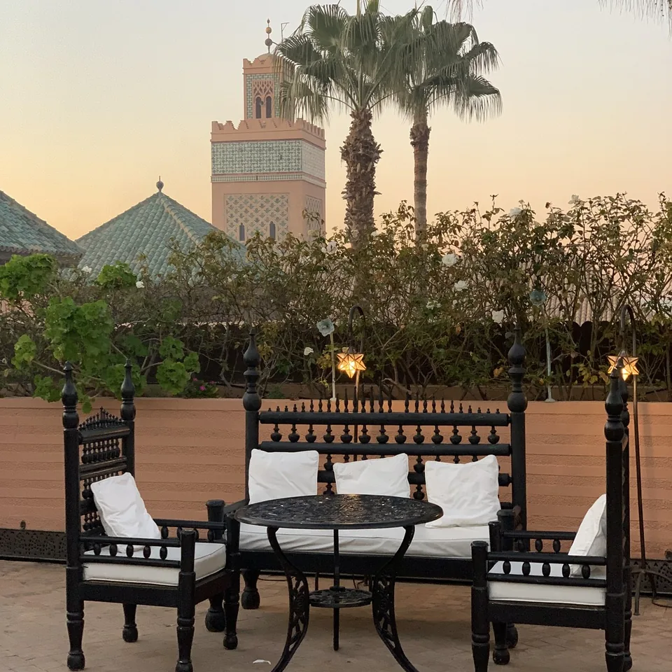 Black carved seating around a table on the roof terrace at La Sultana with the minaret and palms at sunset