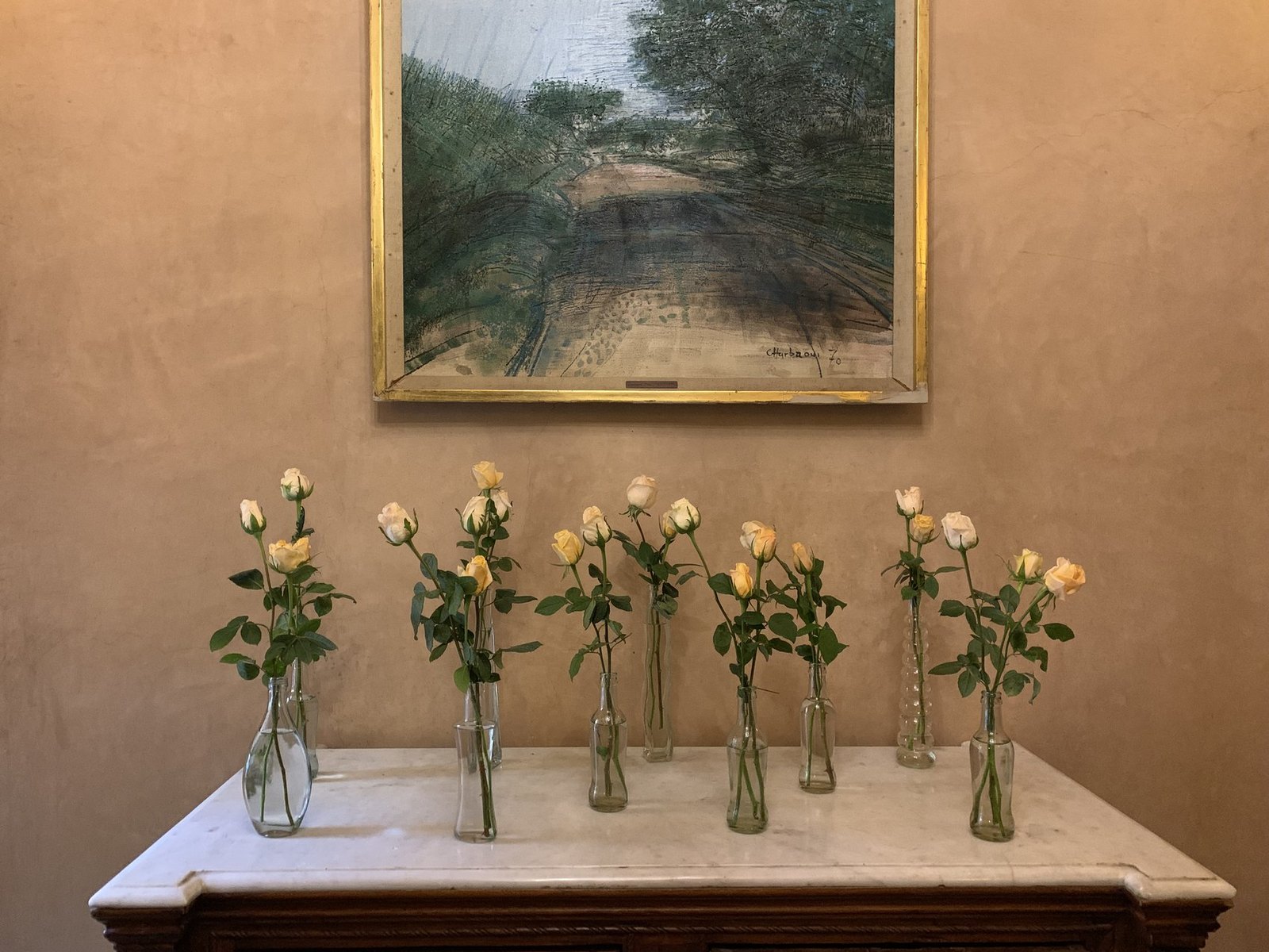 A row of glass bottles each holding a single yellow rose on a console below a framed landscape at La Sultana