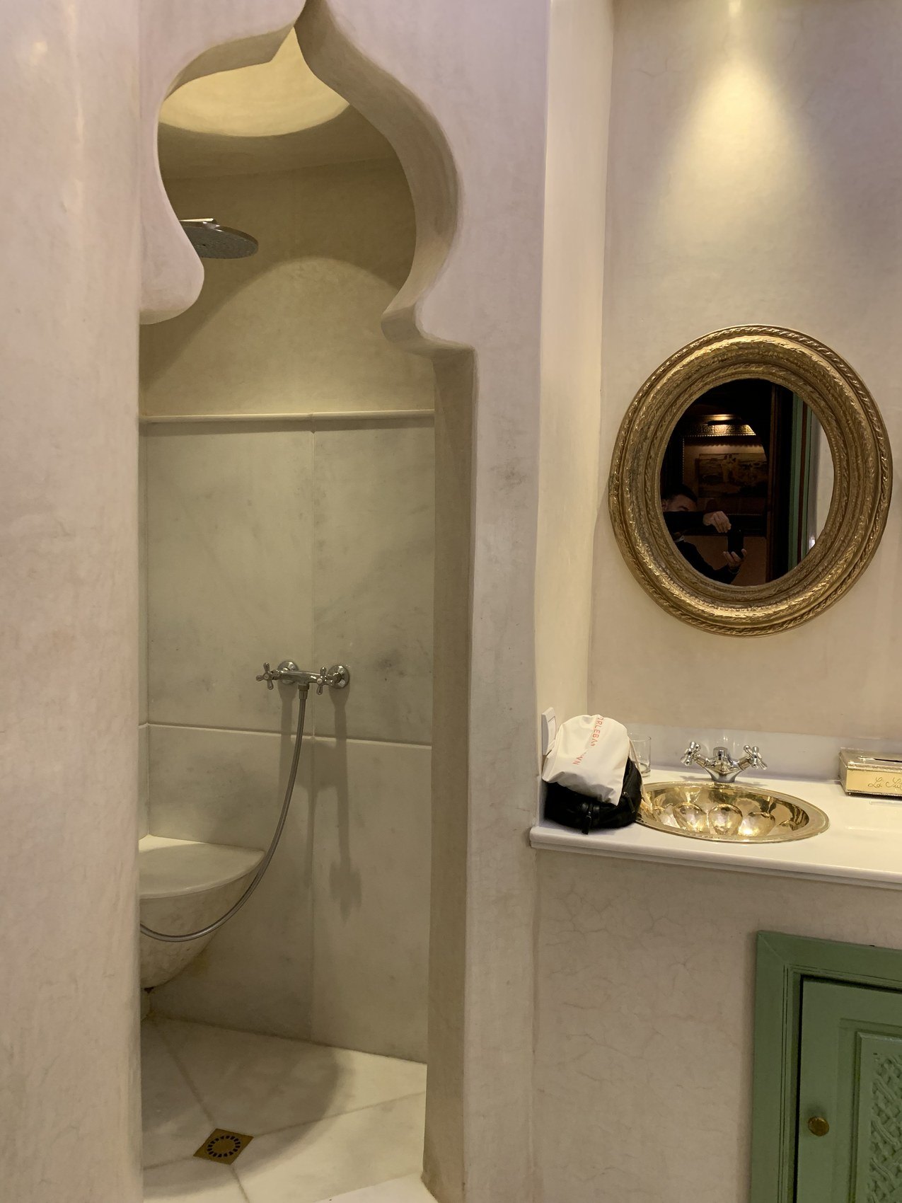 A shower set into a horseshoe arched niche at La Sultana beside a round gilt mirror and a stone basin