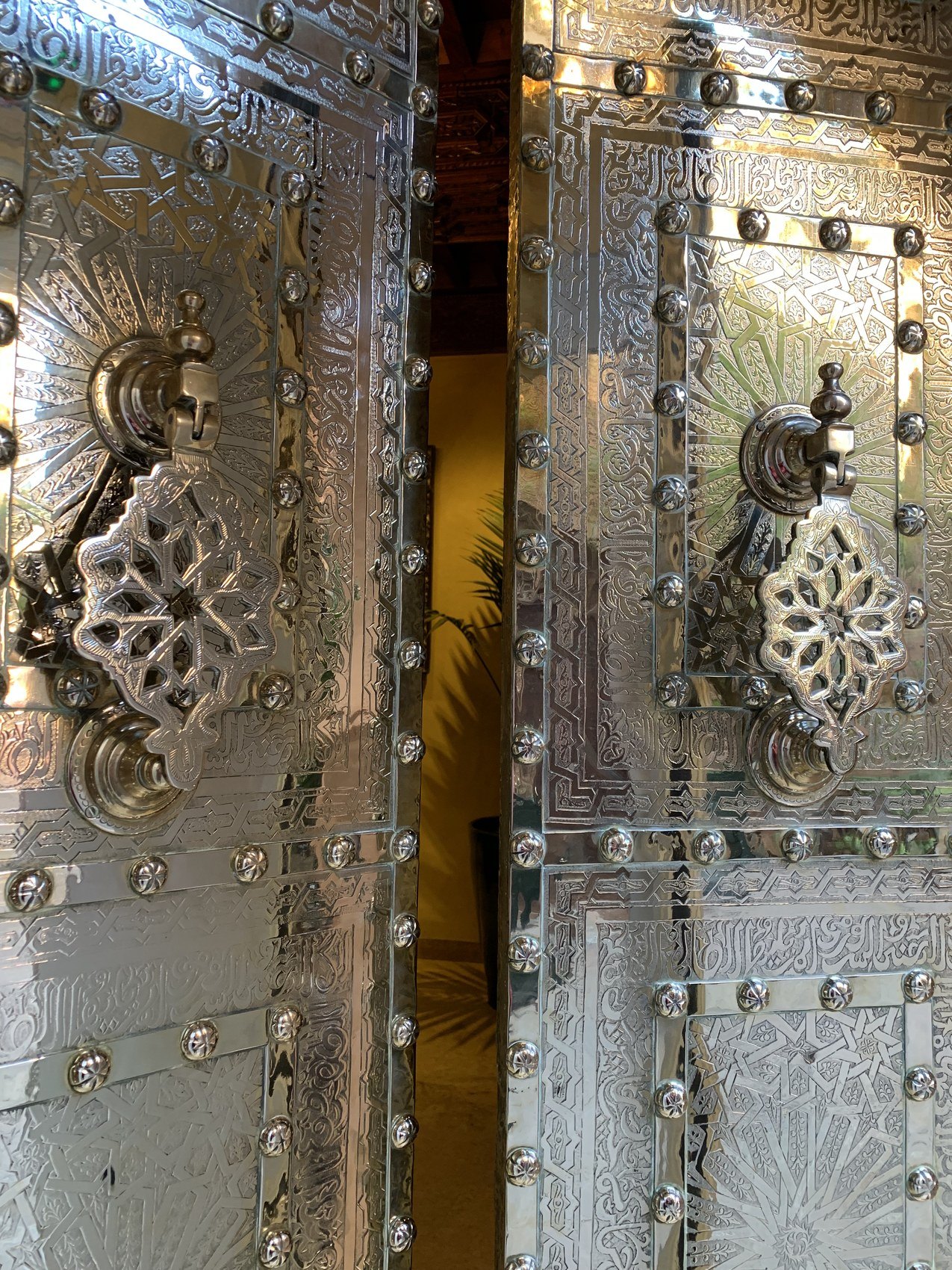 A pair of doors clad in chased silver with heavy ring handles at La Sultana, standing ajar onto a lit room