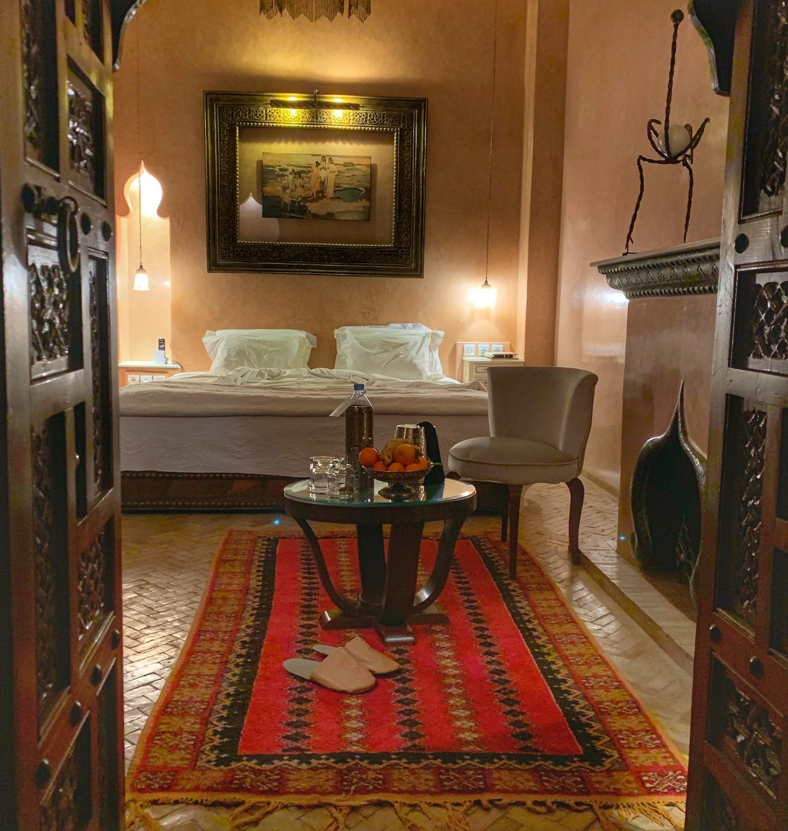 A pair of babouches set side by side on a red patterned rug at the foot of the bed at La Sultana