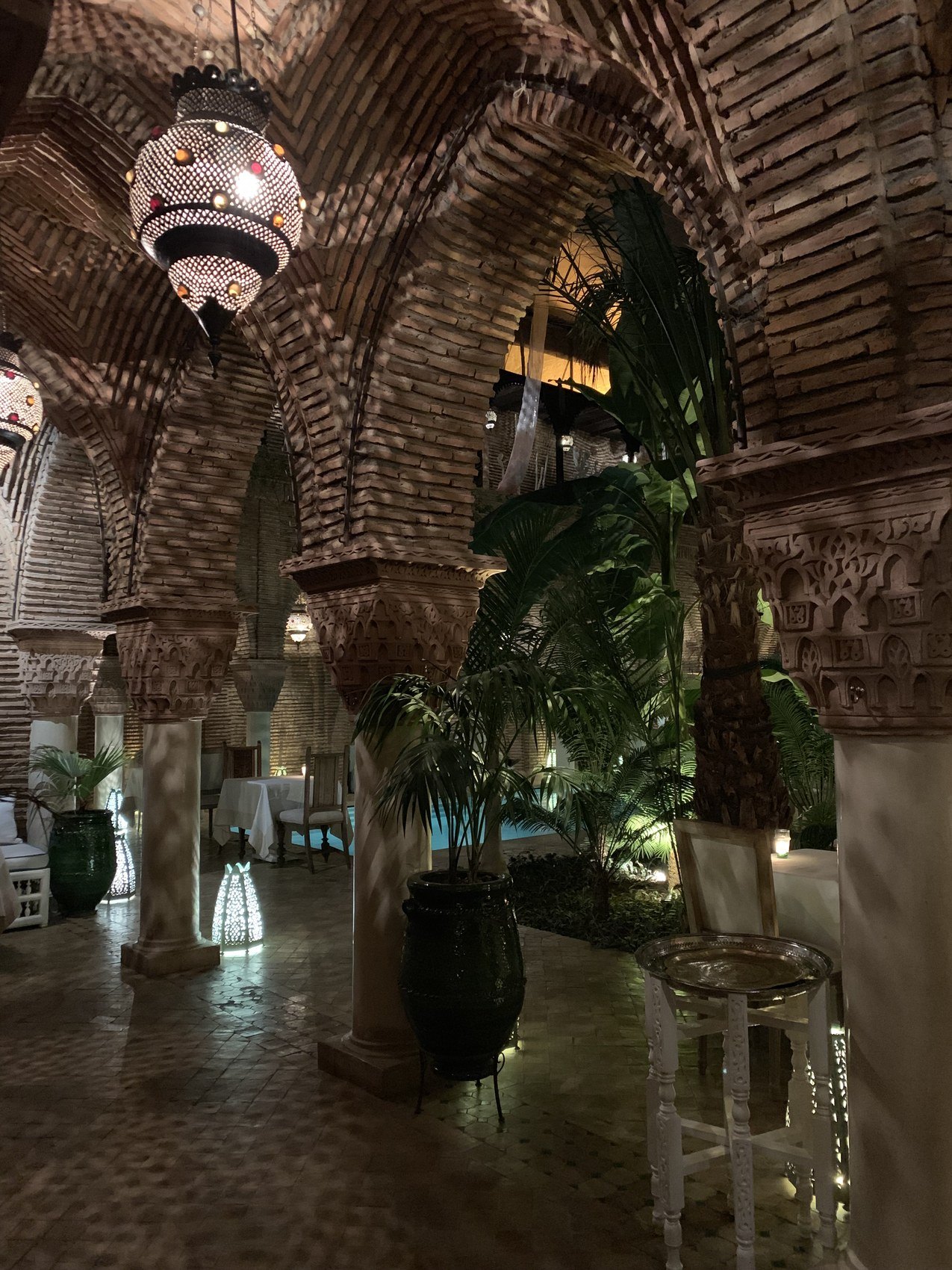 A brick vaulted arcade at La Sultana with carved columns, a pierced metal lantern and tall plants
