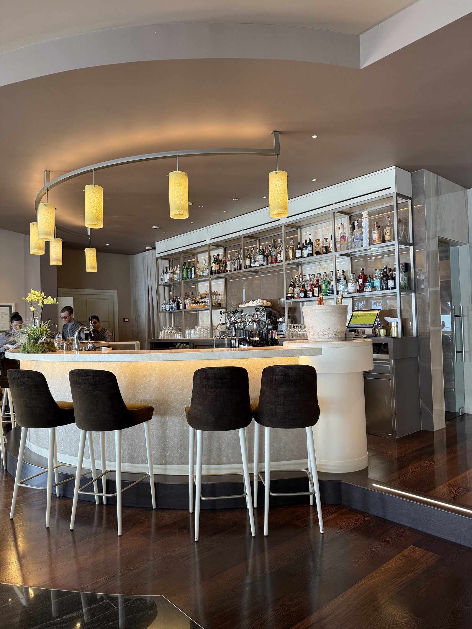 A curved white bar with stools, bottles ranged behind it under pendant lights