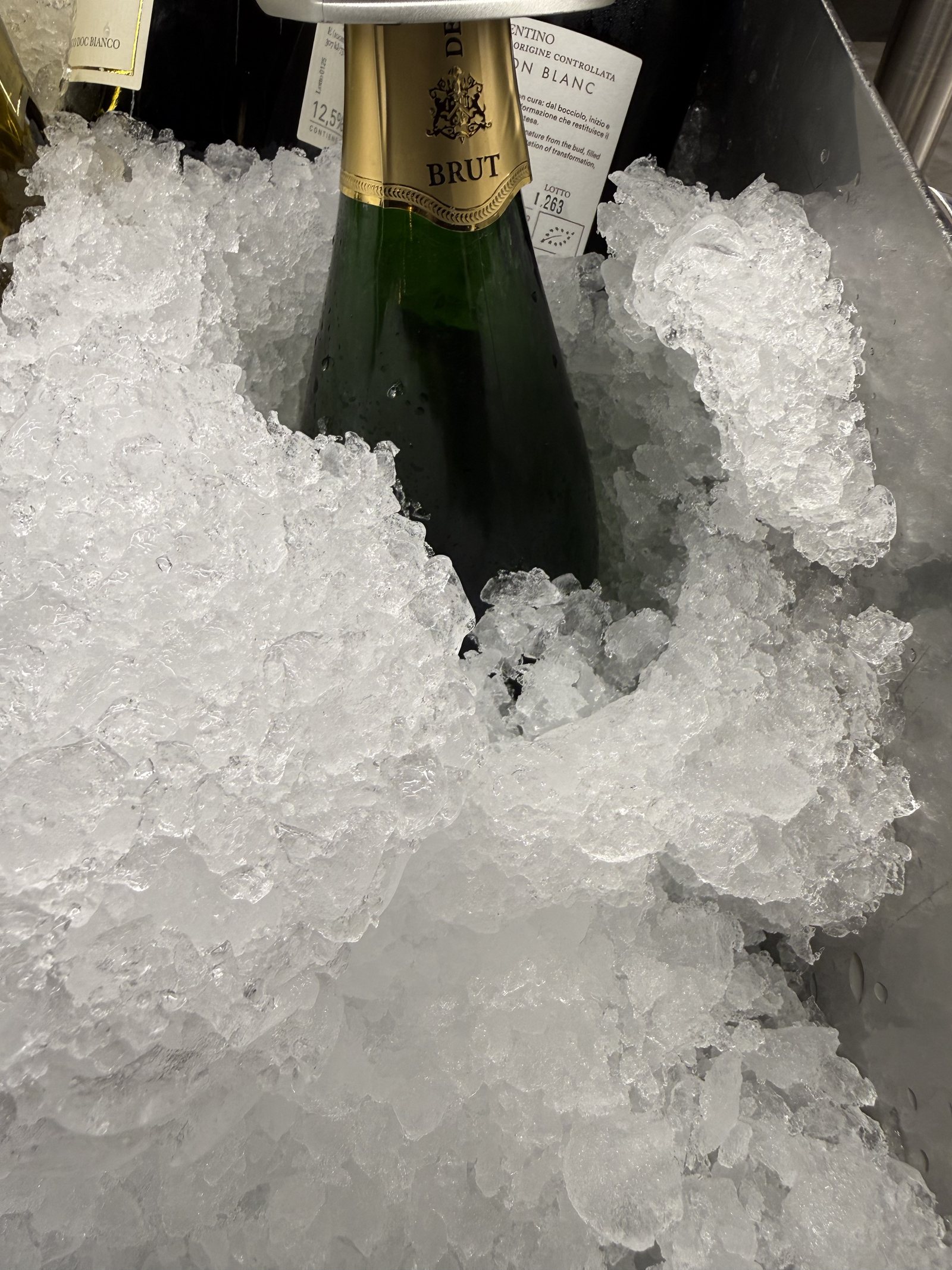 The neck of a bottle of sparkling wine buried in crushed ice