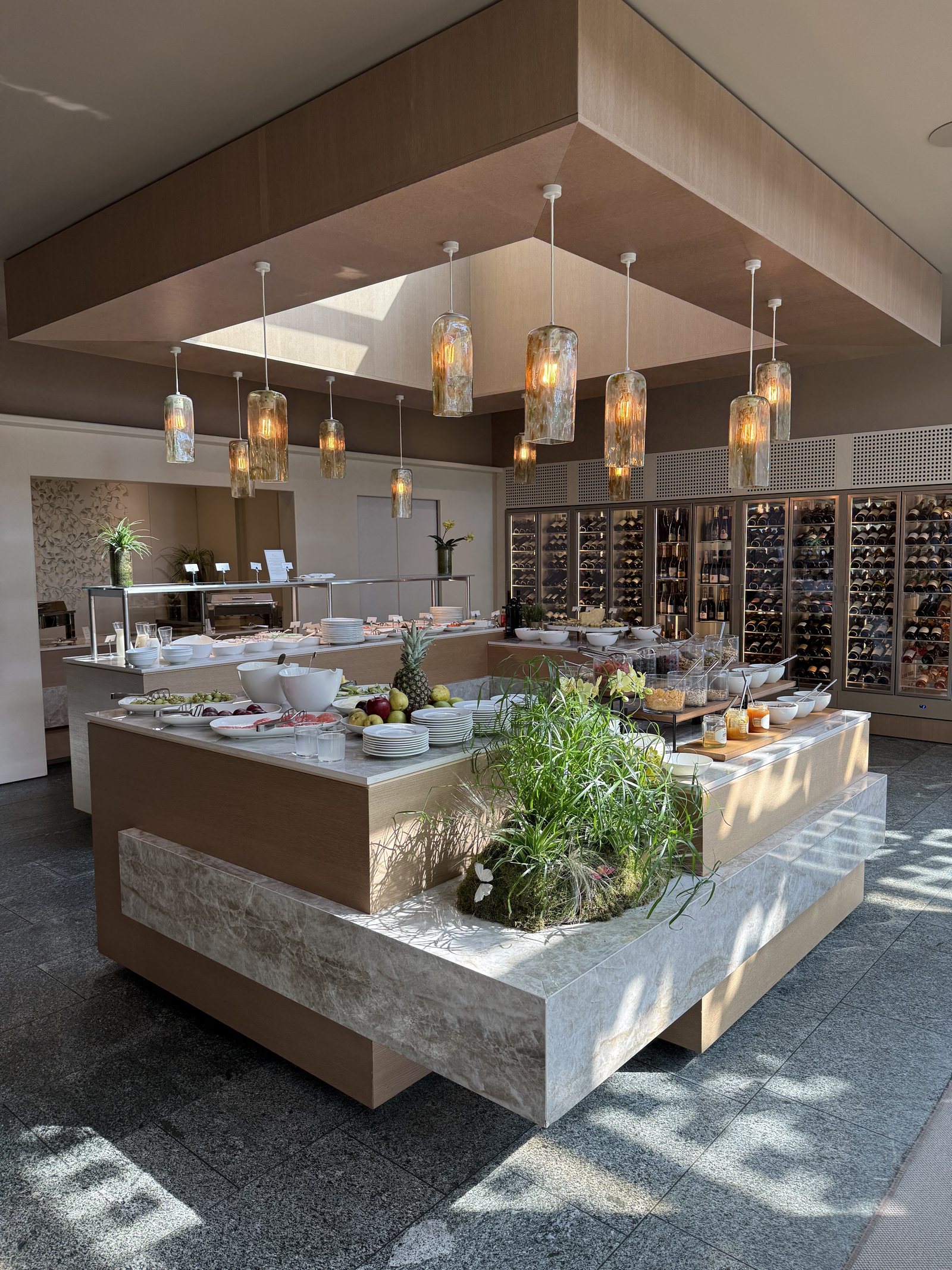 A breakfast buffet on a stone island, with pastries, fruit and herbs under pendant lights
