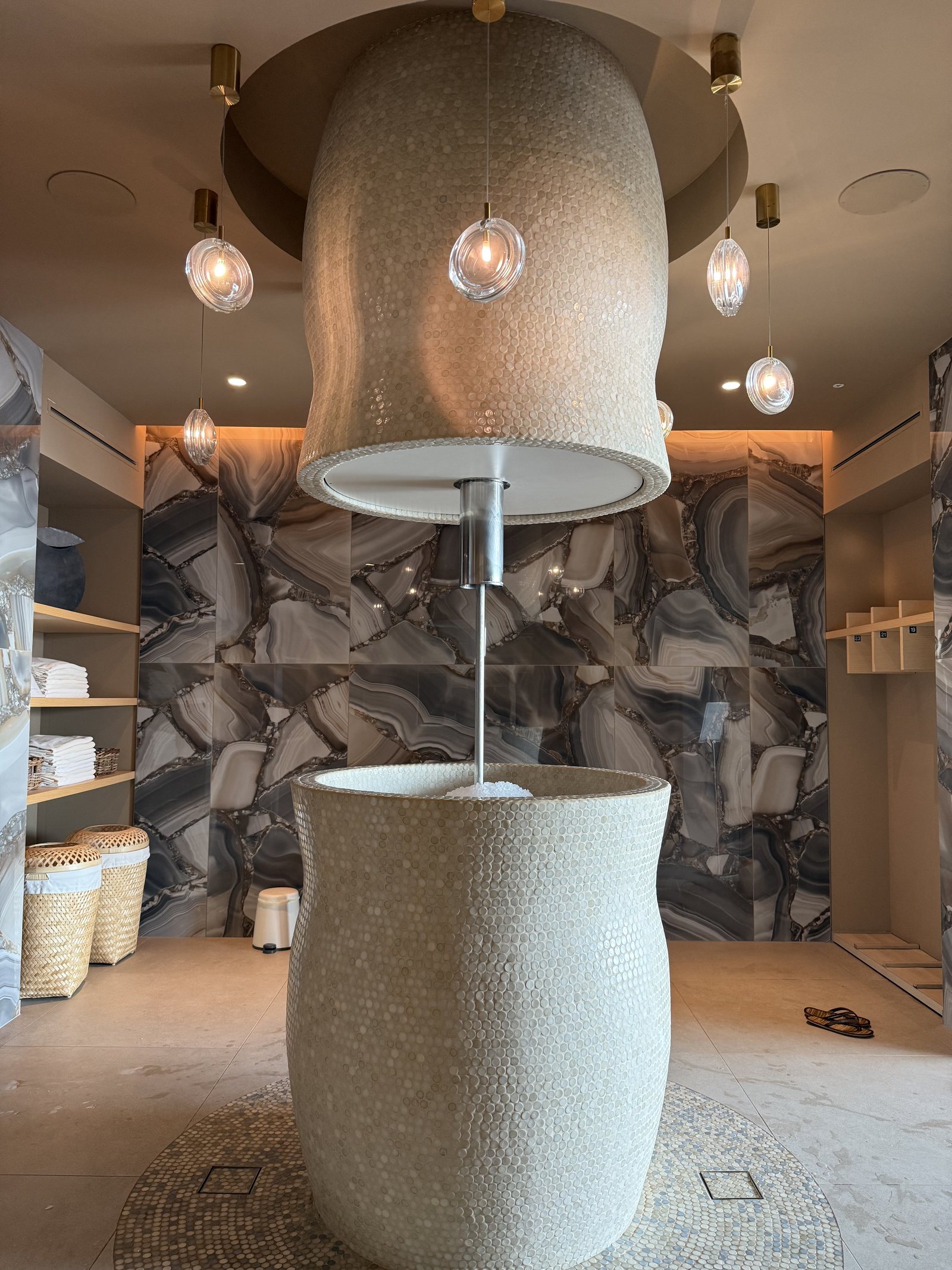 A large ceramic bucket shower hanging in a tiled alcove under pendant lights