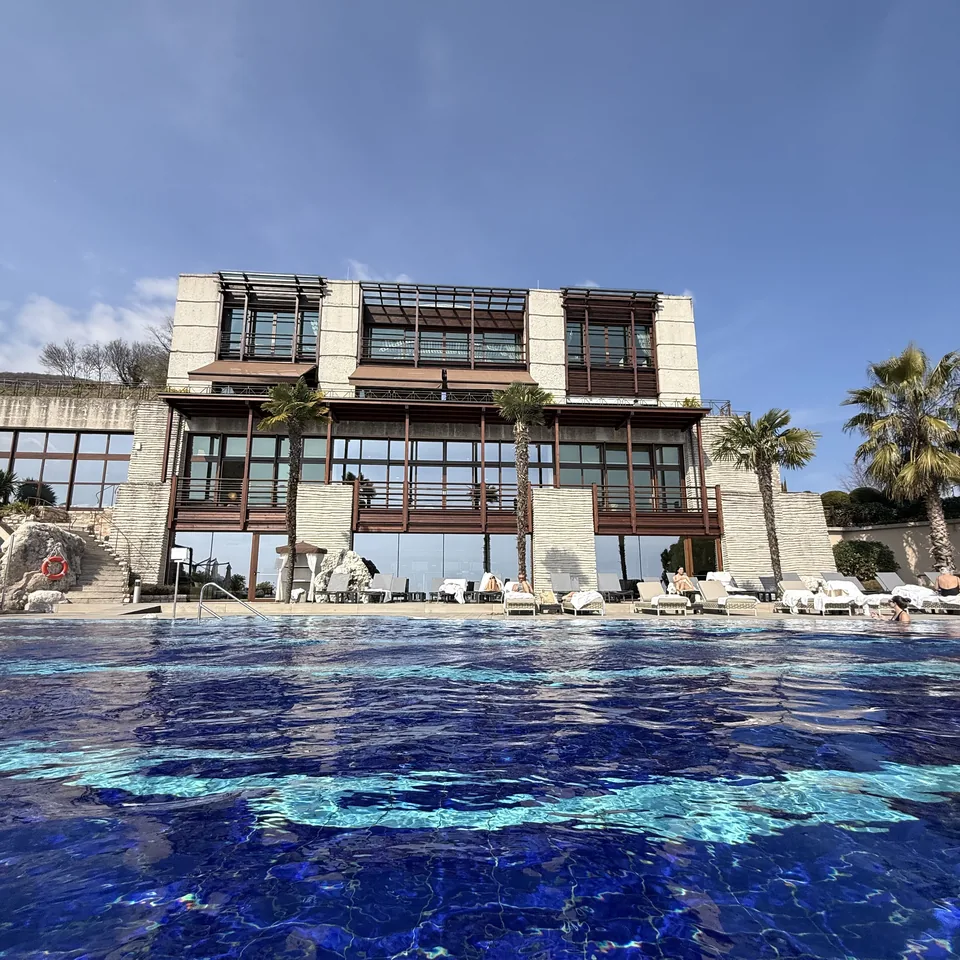 The stone and timber facade of the resort seen across the blue water of the outdoor pool