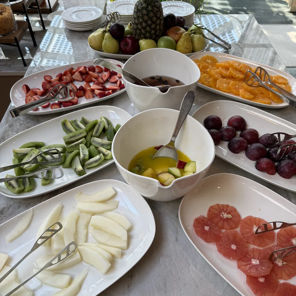 A buffet of cut fruit in white dishes, with a pineapple and a tiered stand behind