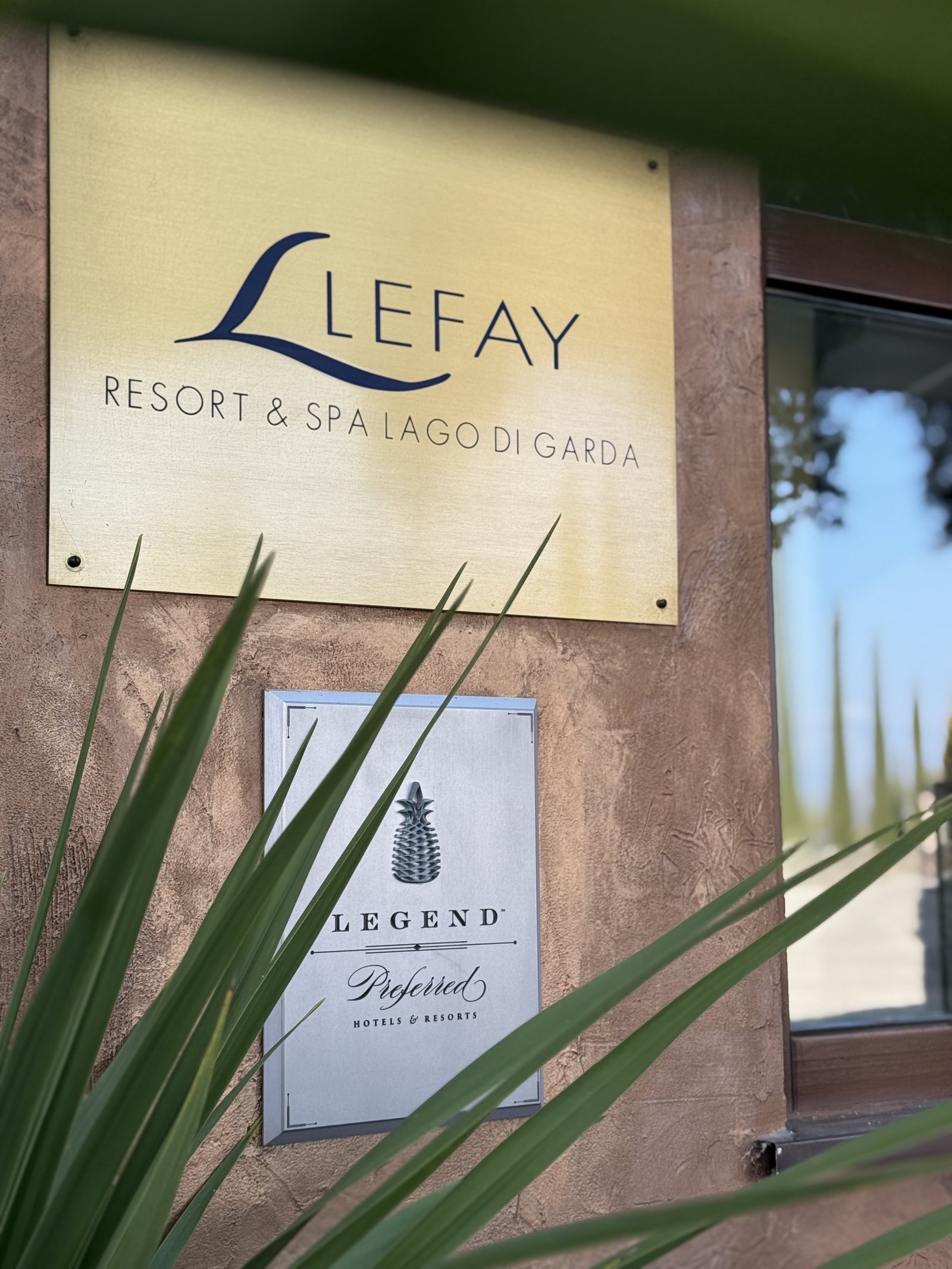 A brass plate reading Lefay Resort and SPA Lago di Garda, mounted on a stone pillar behind a palm