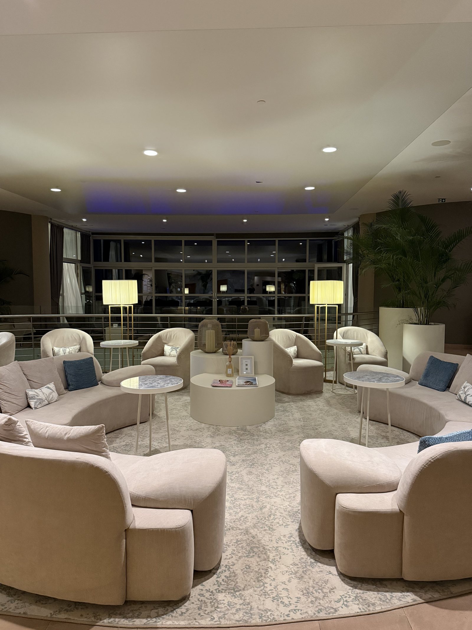 The same kind of room in the evening, lamps lit, chairs drawn round low tables