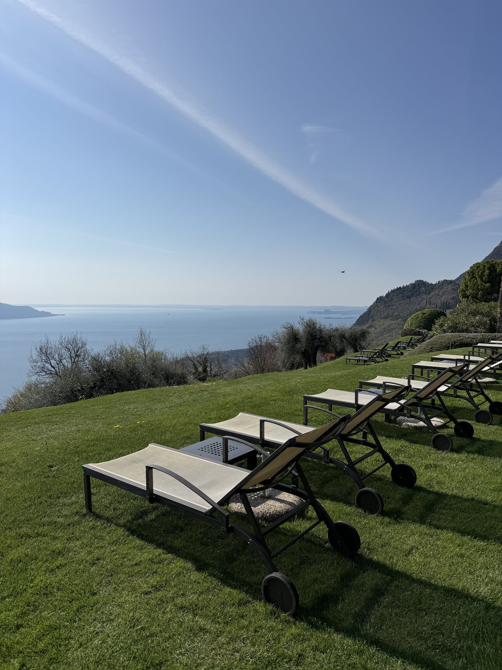 Sun loungers lined up on a lawn above the lake, with the far shore in the distance