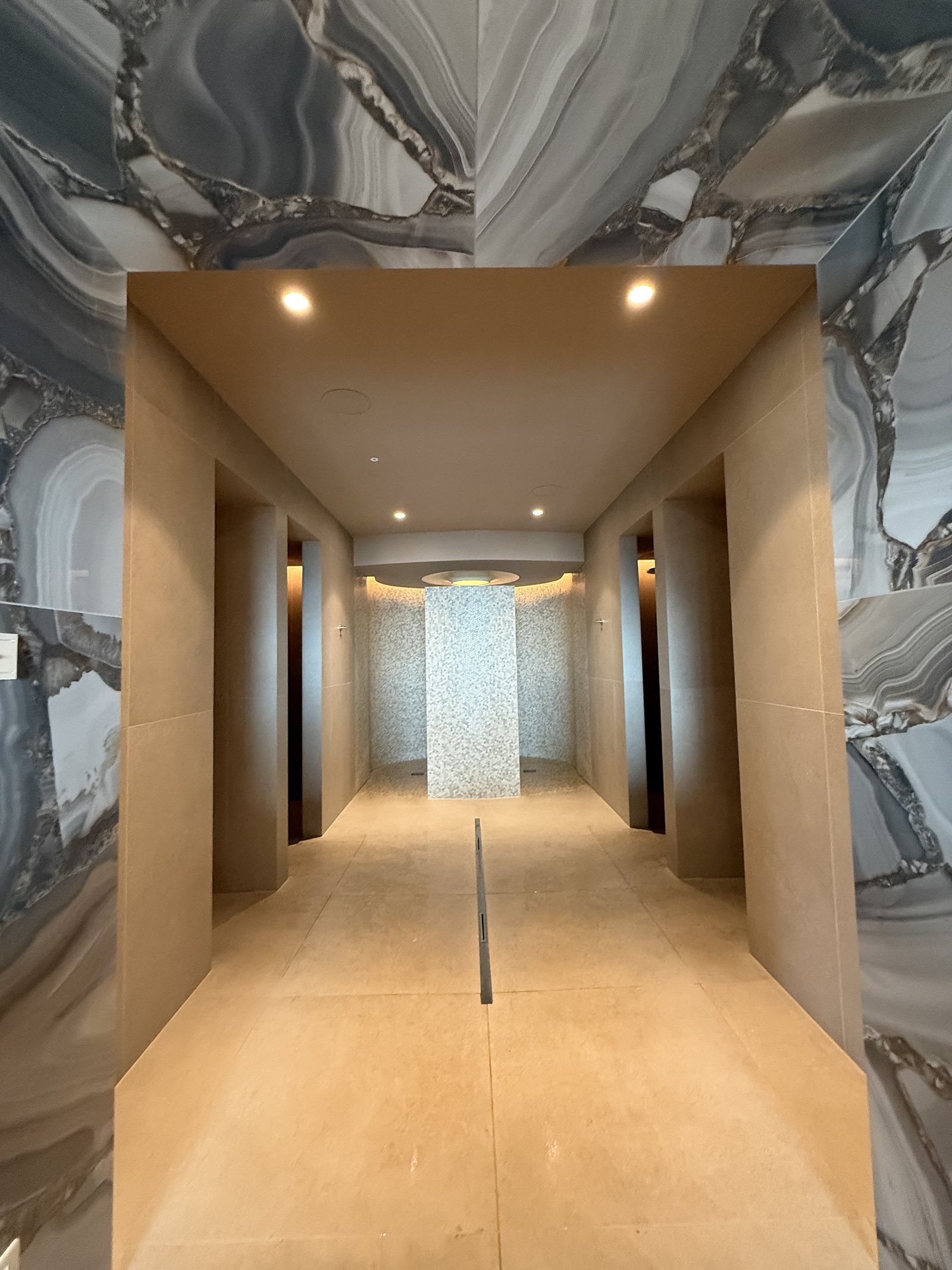 A corridor lined in figured marble leading to a lit mosaic alcove