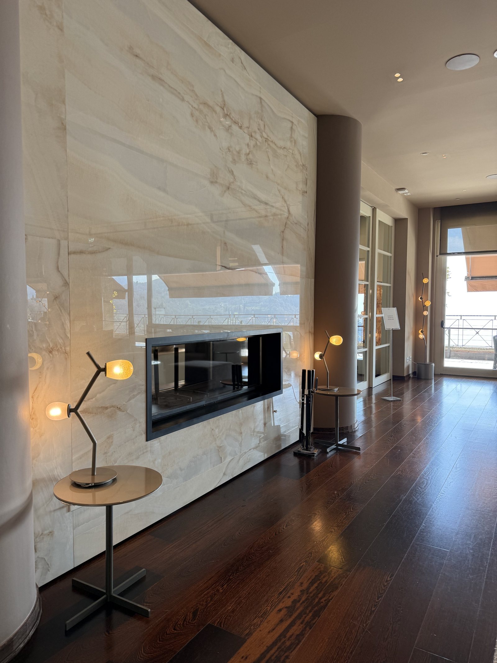 A fireplace set into a wall of backlit onyx, with a side table and lamps beside it