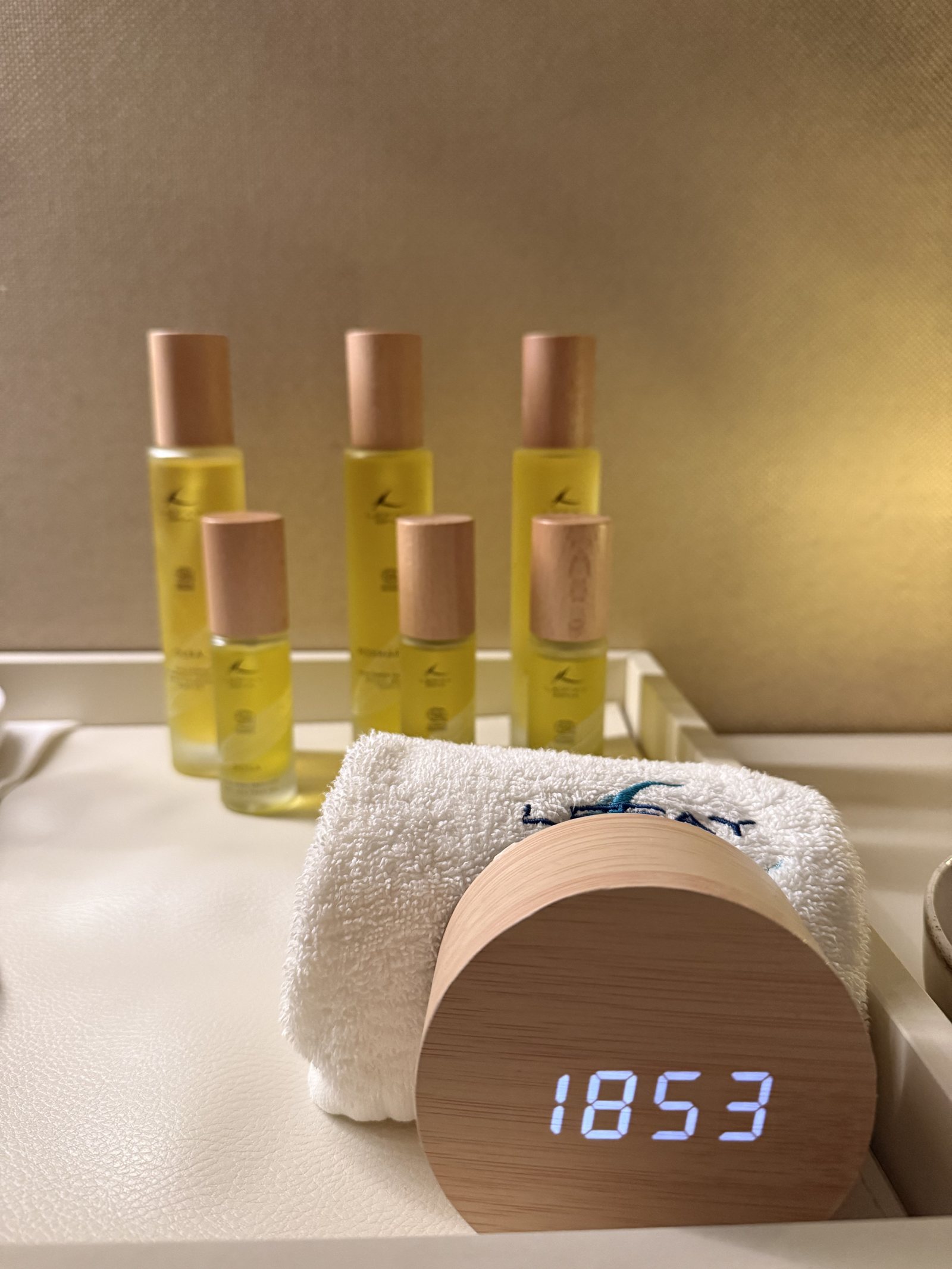 Bottles of oil in a row beside a rolled towel and a small digital clock reading 18:53