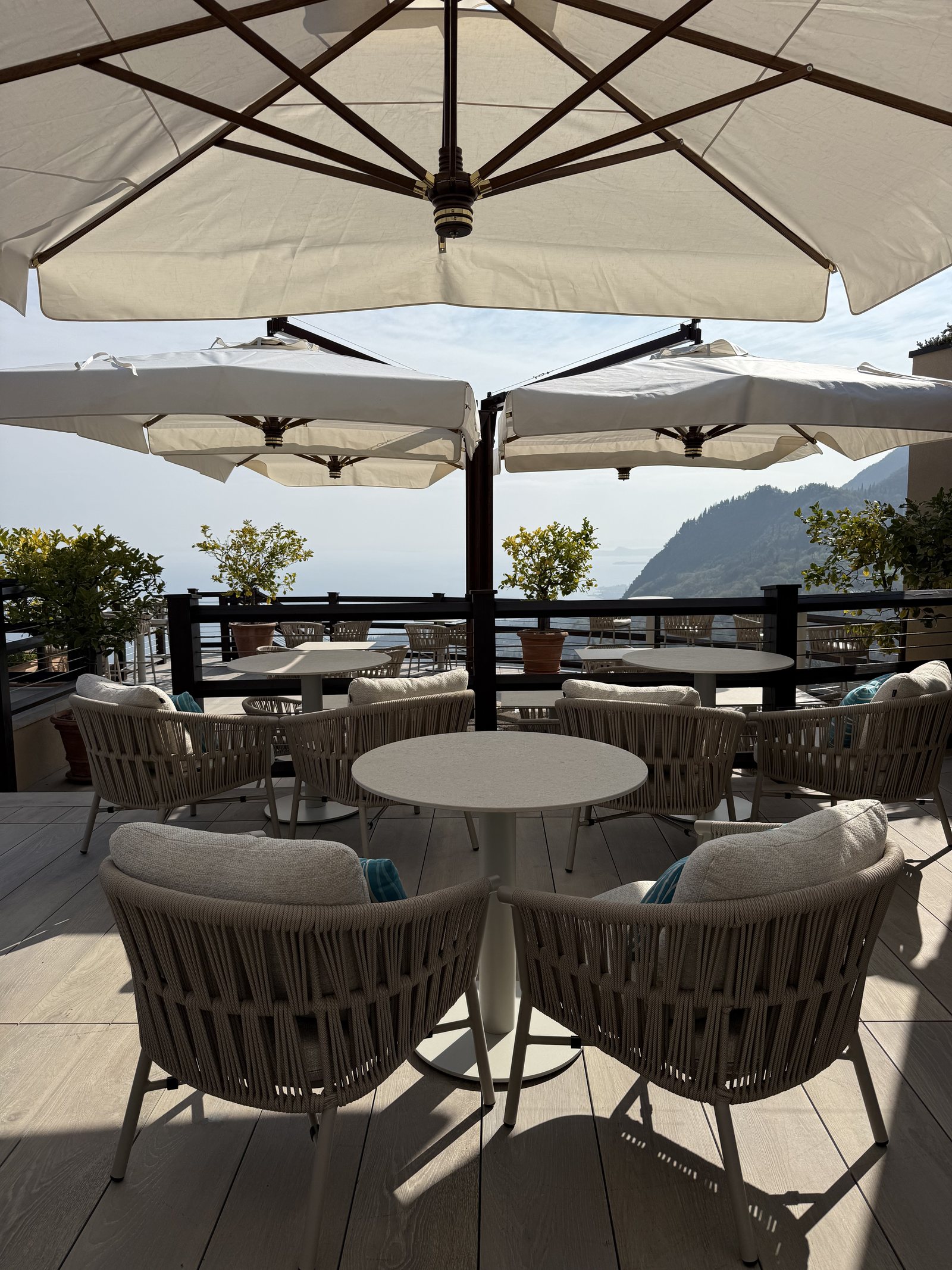 Cream parasols over tables and woven chairs on a timber deck above the lake