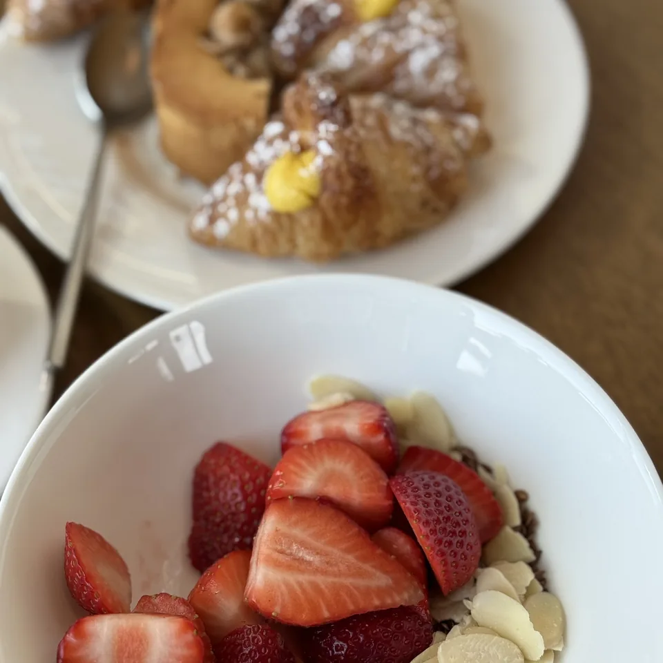Two filled pastries dusted with sugar beside a bowl of strawberries and flaked almonds