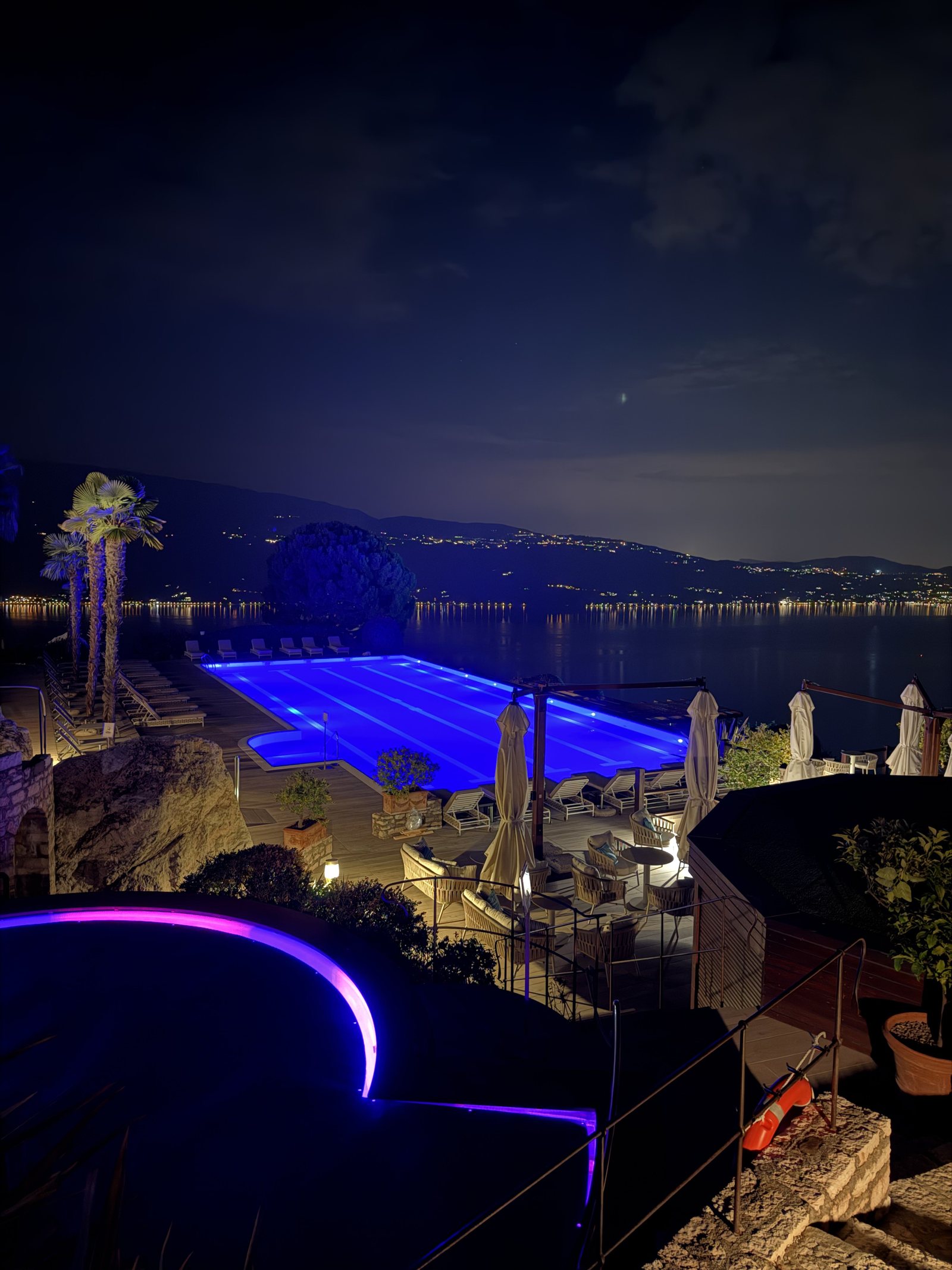The lit pool at night above the lake, with the lights of a town on the far shore