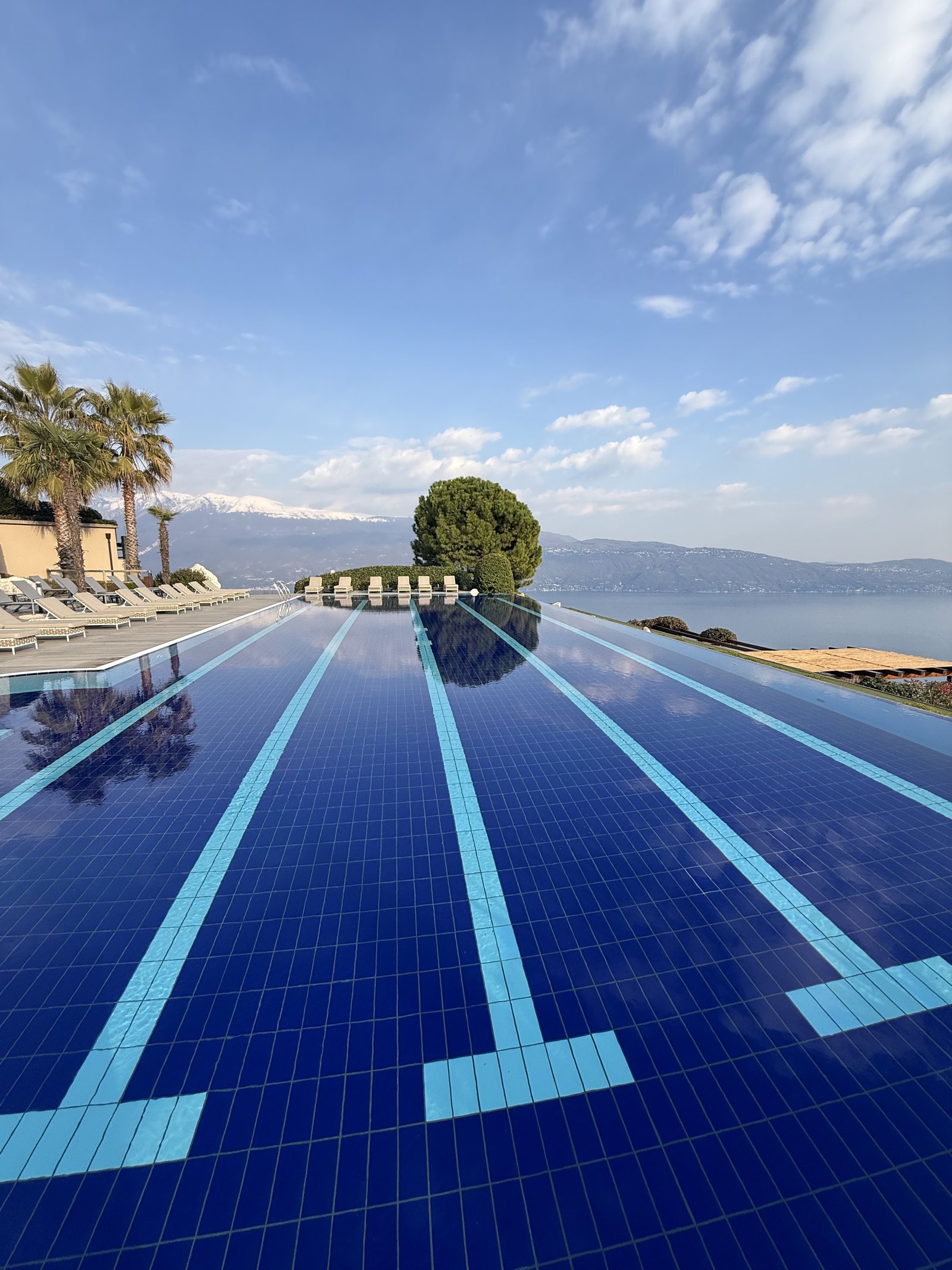 The outdoor pool in two tones of blue tile, photographed along its length towards the far edge