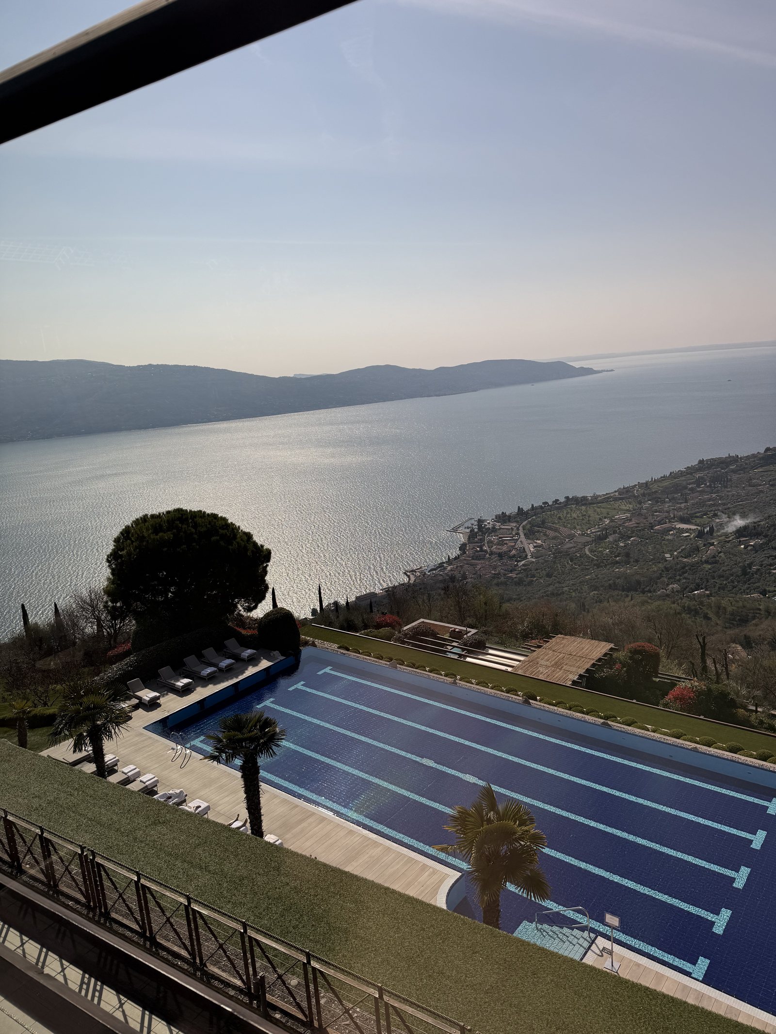 The outdoor pool and its deck seen from a window above, with the lake filling the background