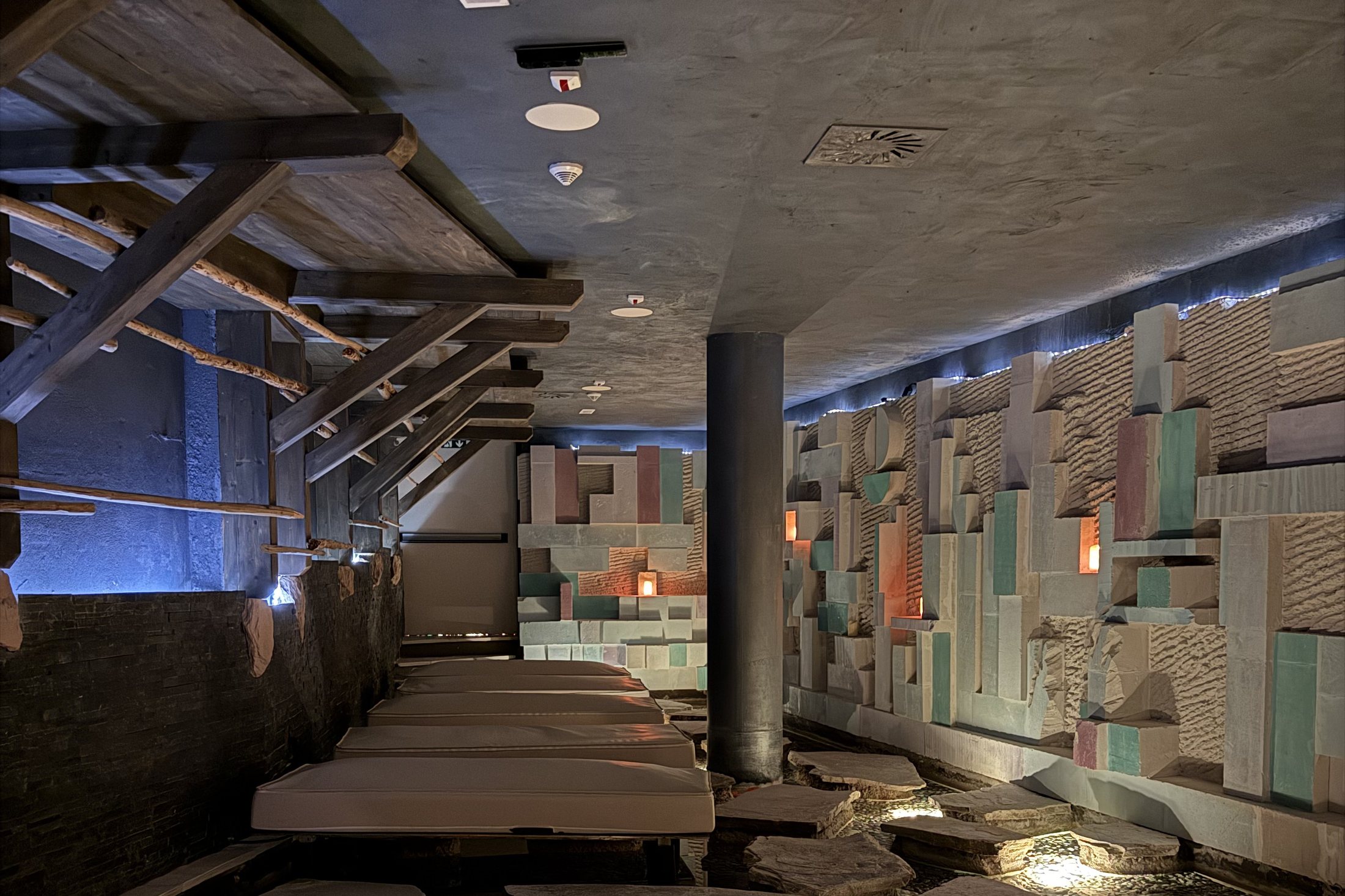 A relaxation area with beds along a wall of coloured panels, above a bed of lit stones and water