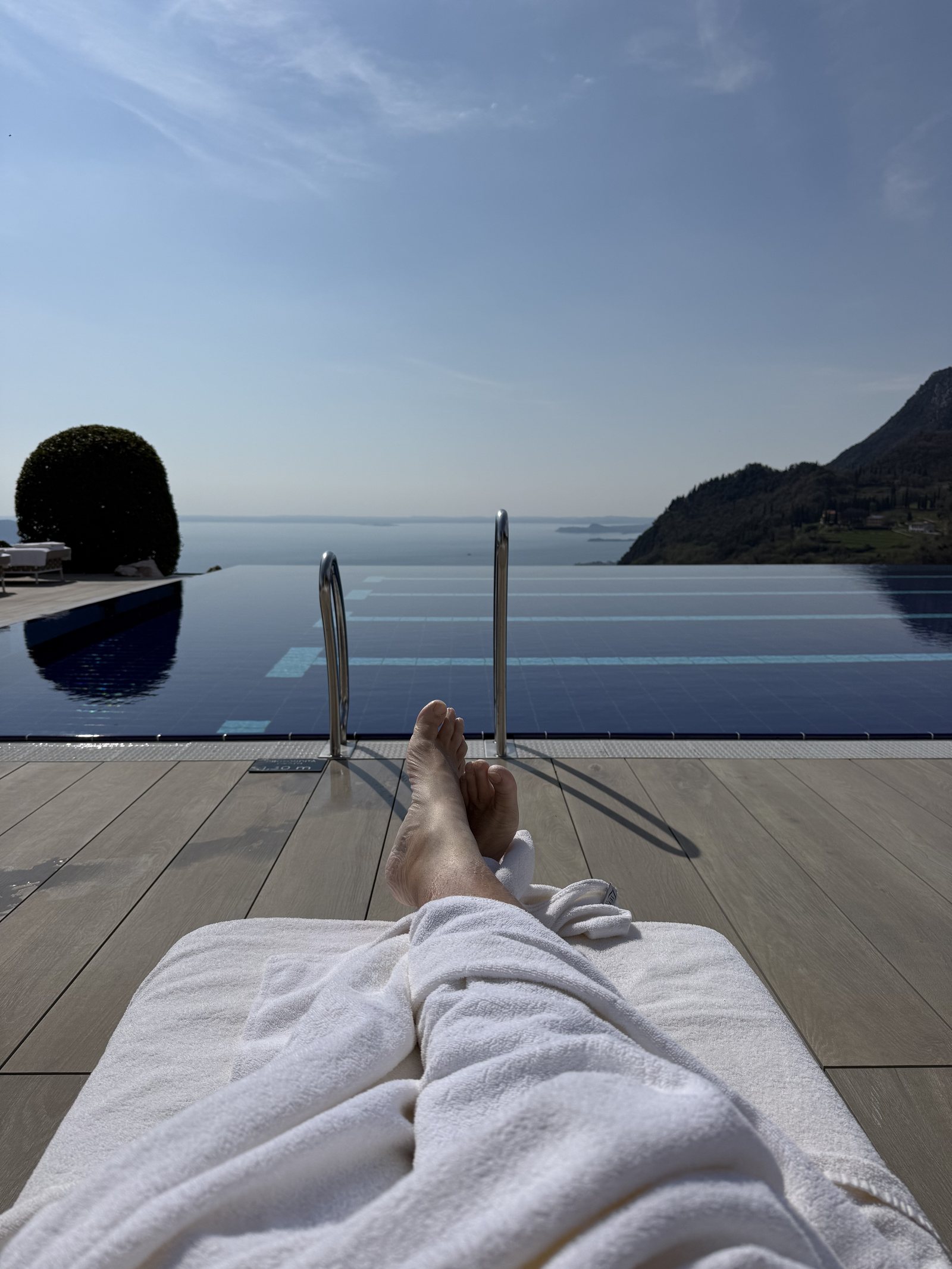 A view along a white robe and bare feet towards the pool edge and the lake