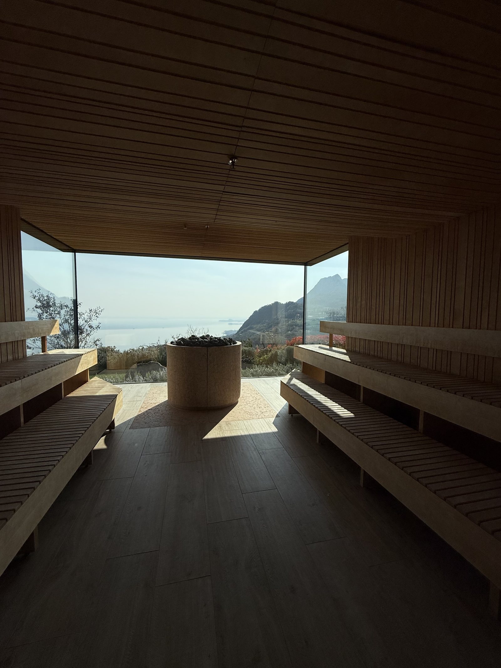 A dark timber sauna with low benches, the glass end wall looking down to the water