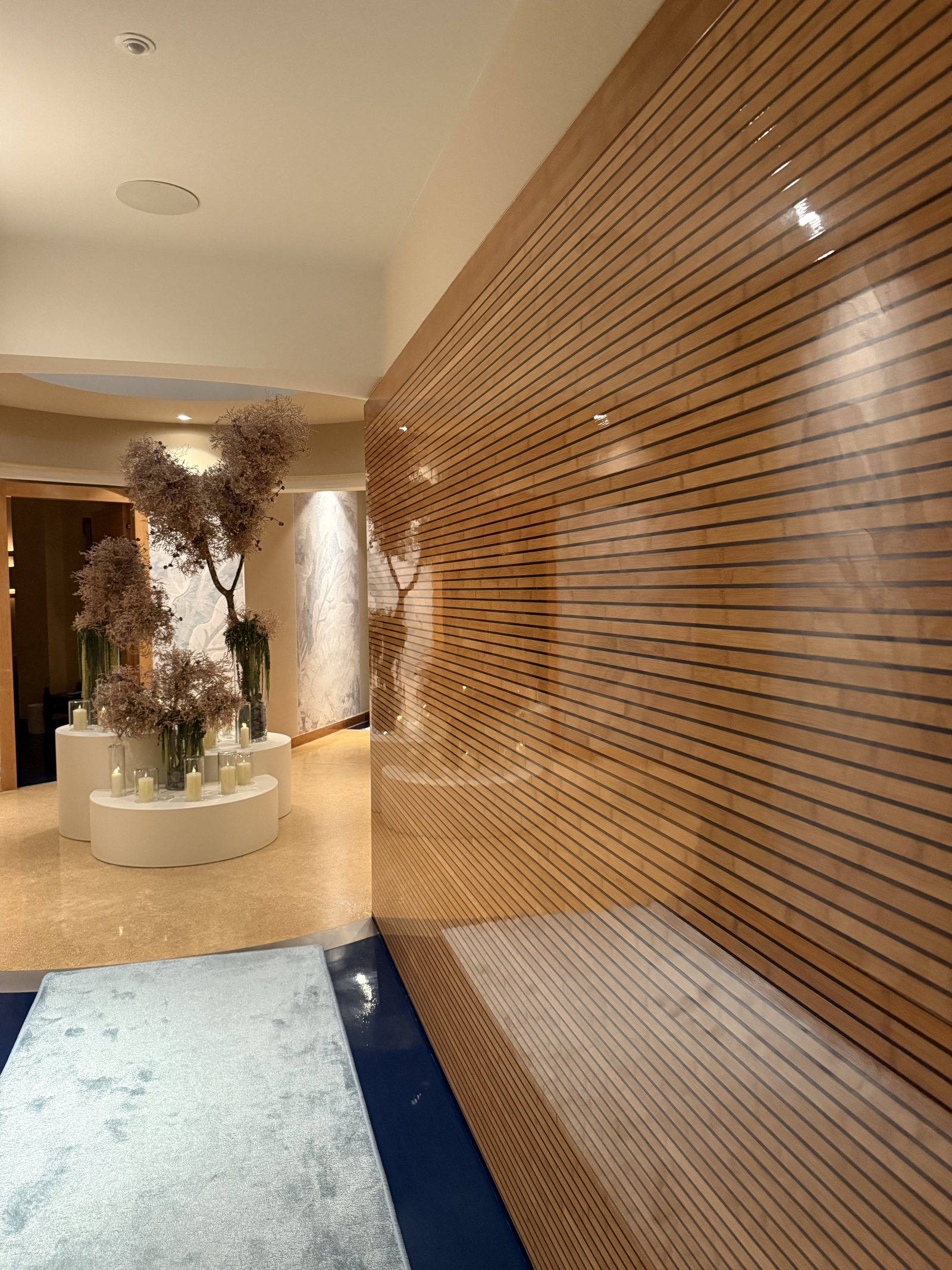 A slatted timber corridor opening onto a lit space with dried flowers