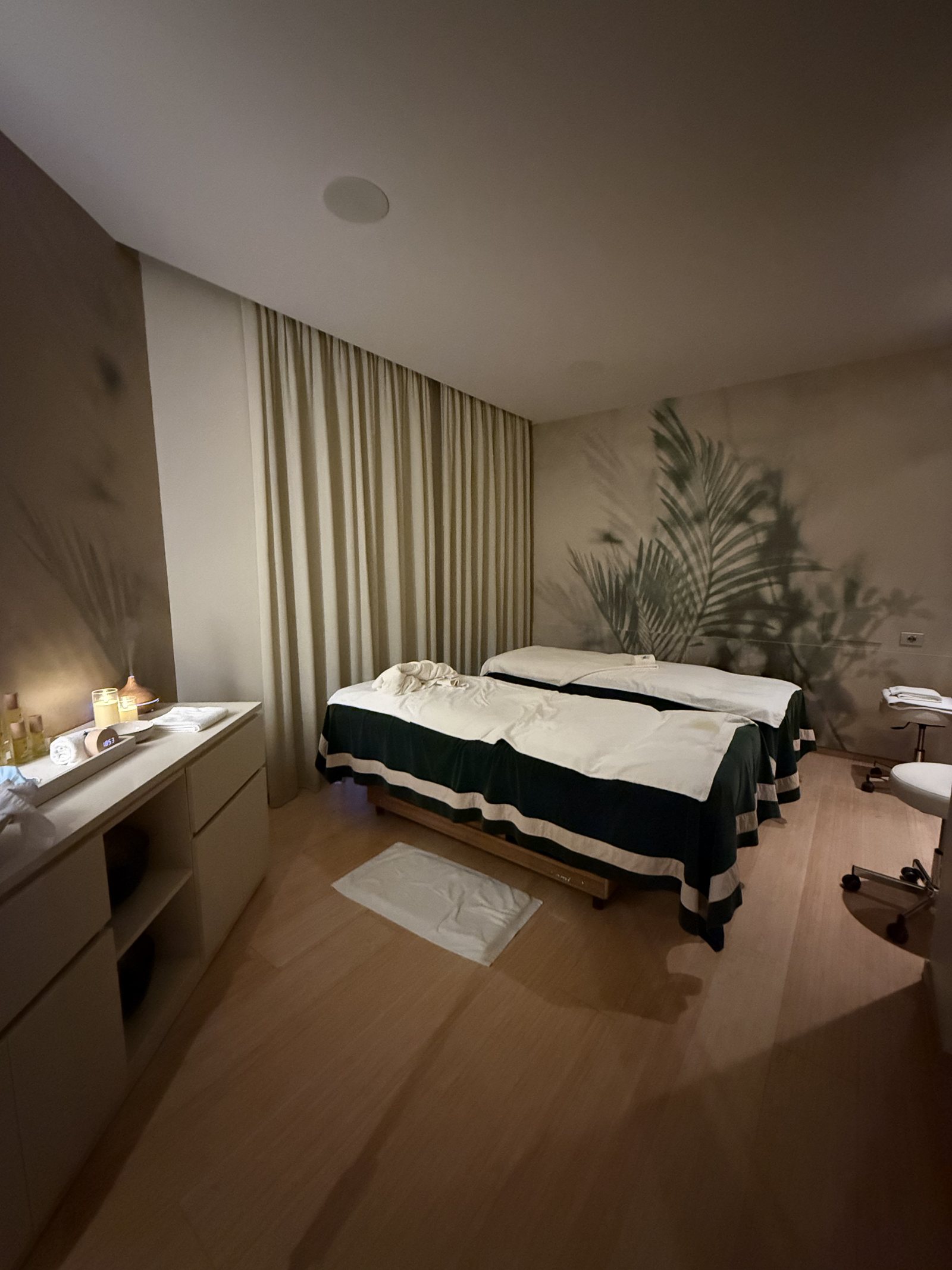 A treatment room with a single bed made up in green and white, candles and a dark window