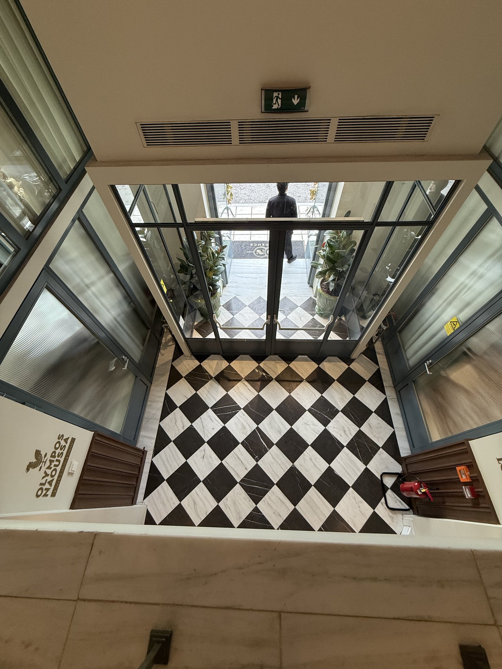 A black and white diamond-tiled floor seen from several storeys above, down a glazed lightwell
