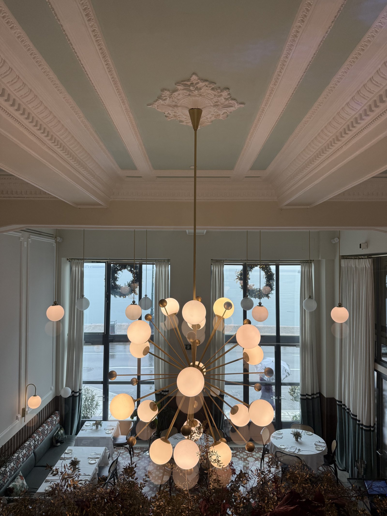 A large globe chandelier in a coffered white room with tall windows onto the sea behind it