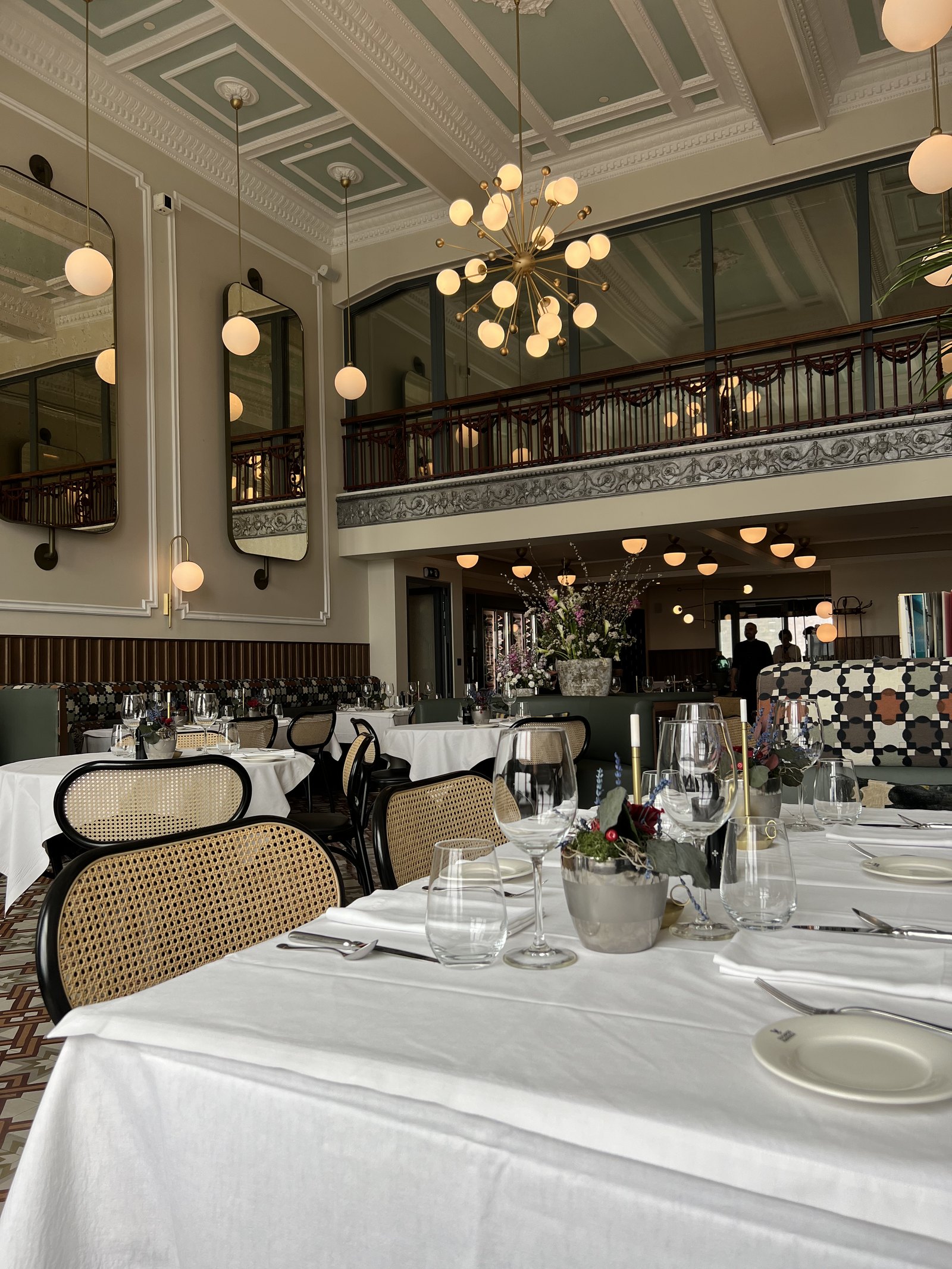 The dining room from the other end, globes at two heights, the mezzanine above and tables laid in white linen