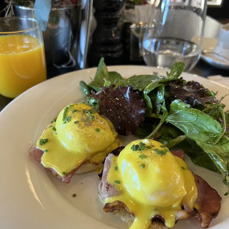 Eggs benedict on toasted bread with rocket and ham, beside a glass of orange juice