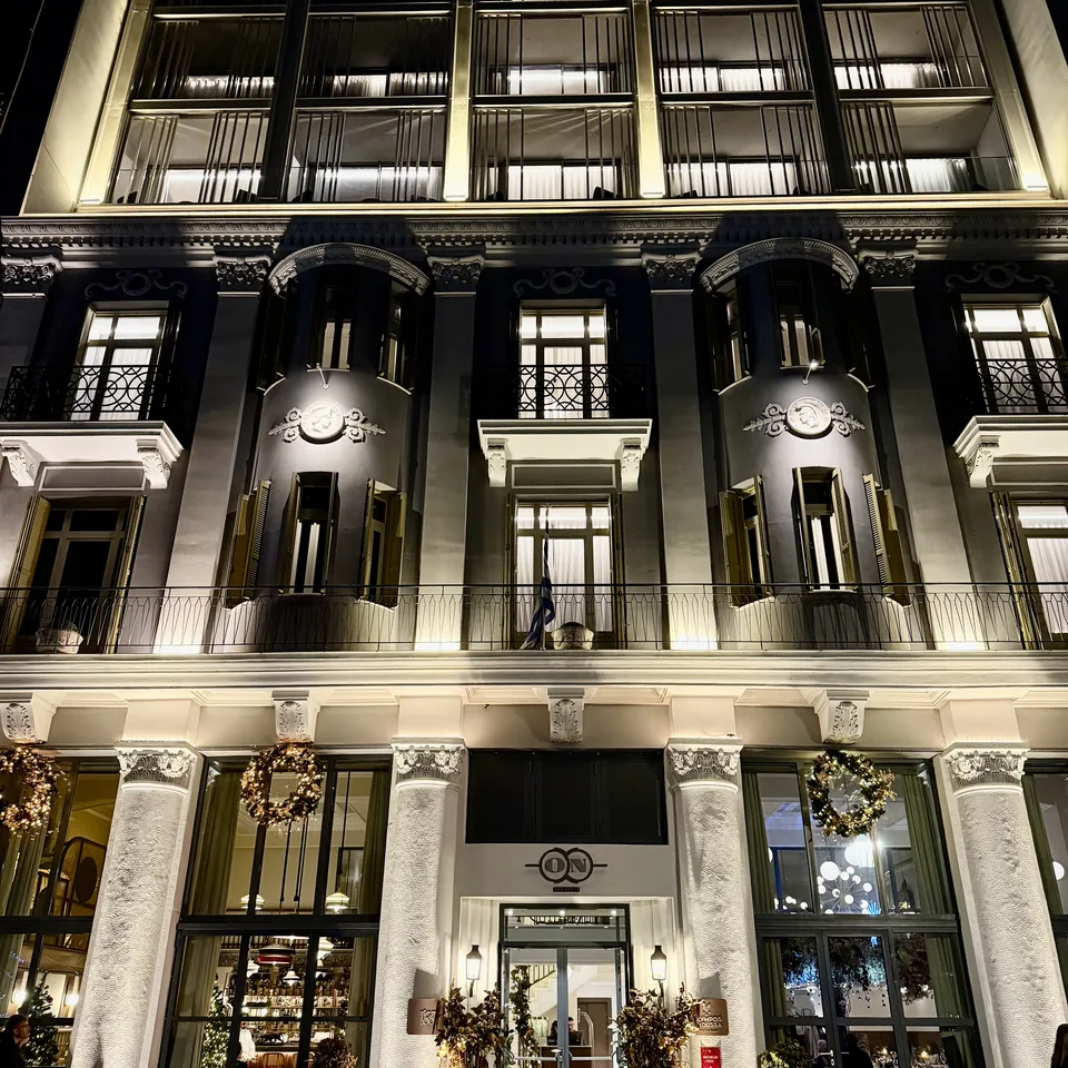 The lit 1926 facade on Leoforos Nikis at night, columns and tall windows with Christmas wreaths across the ground floor