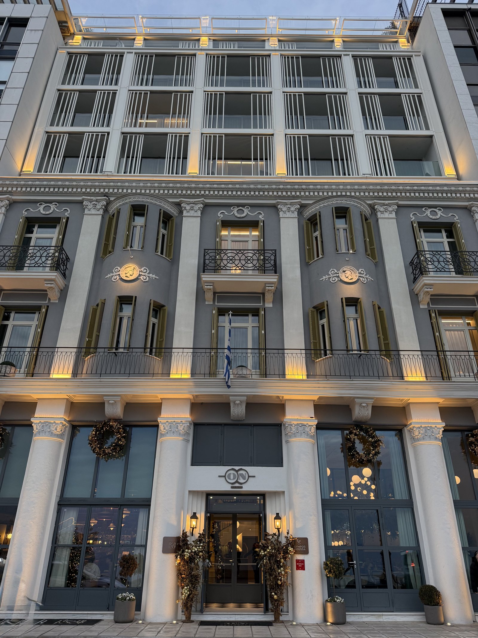 The 1926 facade at dusk, columns and tall windows with Christmas wreaths hung along the ground floor