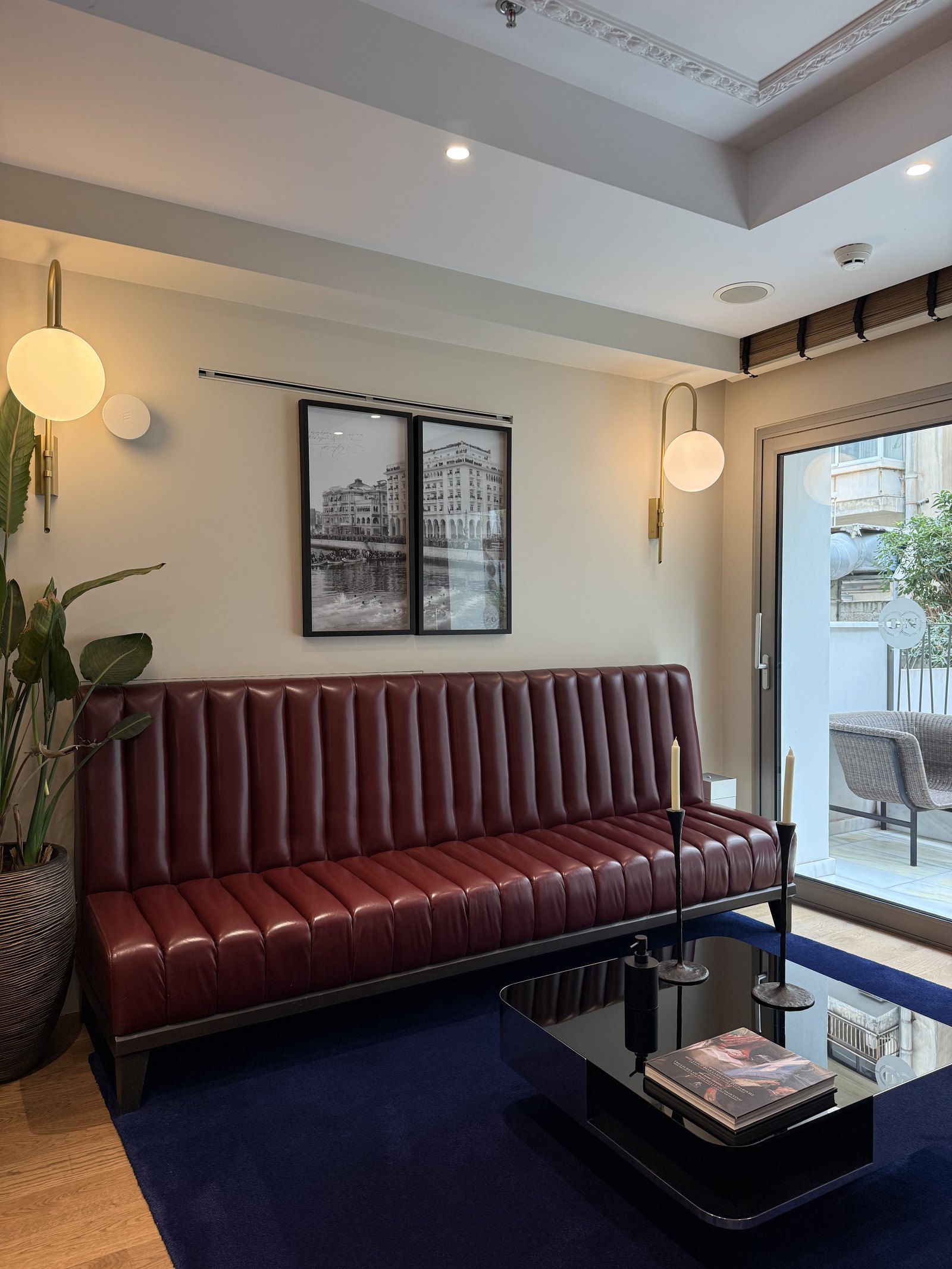 An oxblood leather banquette under a framed black and white photograph, globe sconces either side and a blue rug below