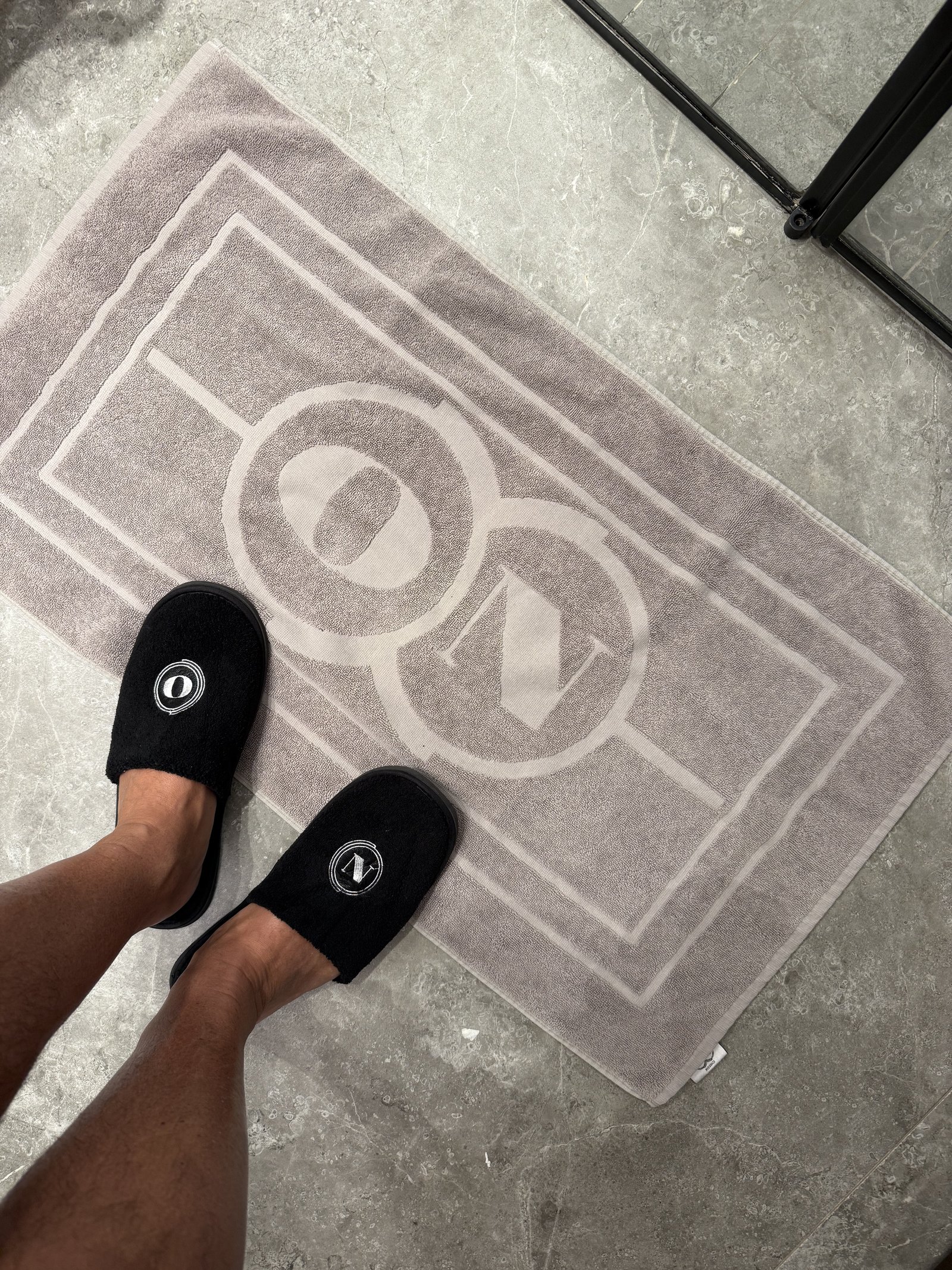Slippers on a grey bath mat woven with the ON monogram, feet in them