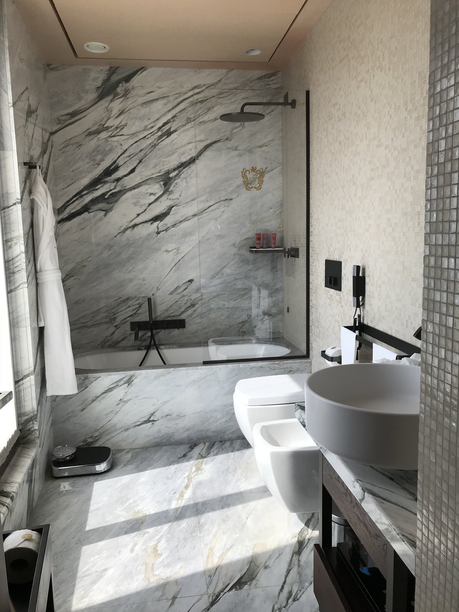 A bathroom in white Calacatta marble with a round basin, a walk-in bath and a rain shower over it