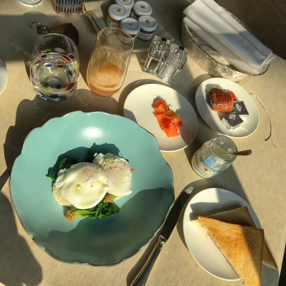 A breakfast table from above: poached eggs on spinach on a green plate, smoked salmon, toast and coloured Murano glasses