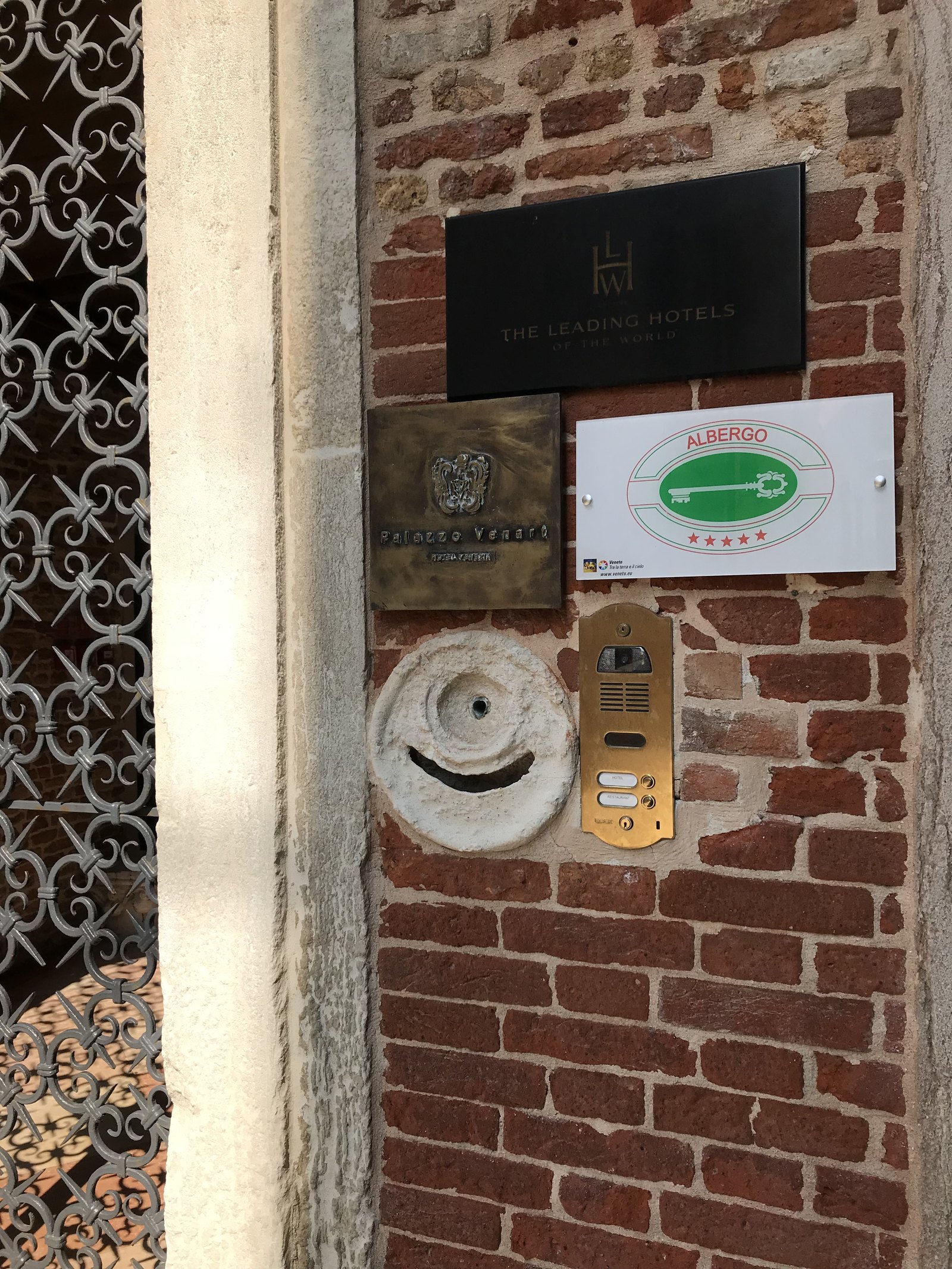 A brass plate reading Palazzo Venart on a brick wall beside a Leading Hotels of the World plate and a five-star albergo sign