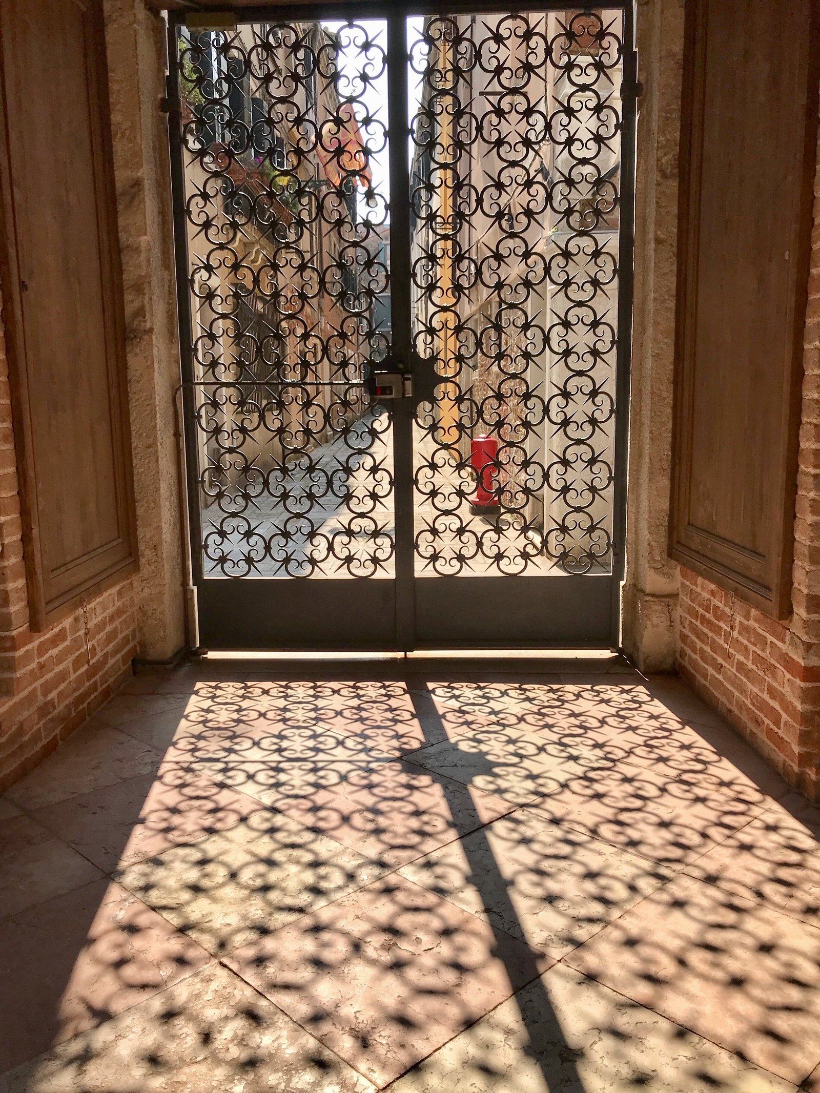 A wrought-iron double gate throwing a lace of shadow across a stone floor