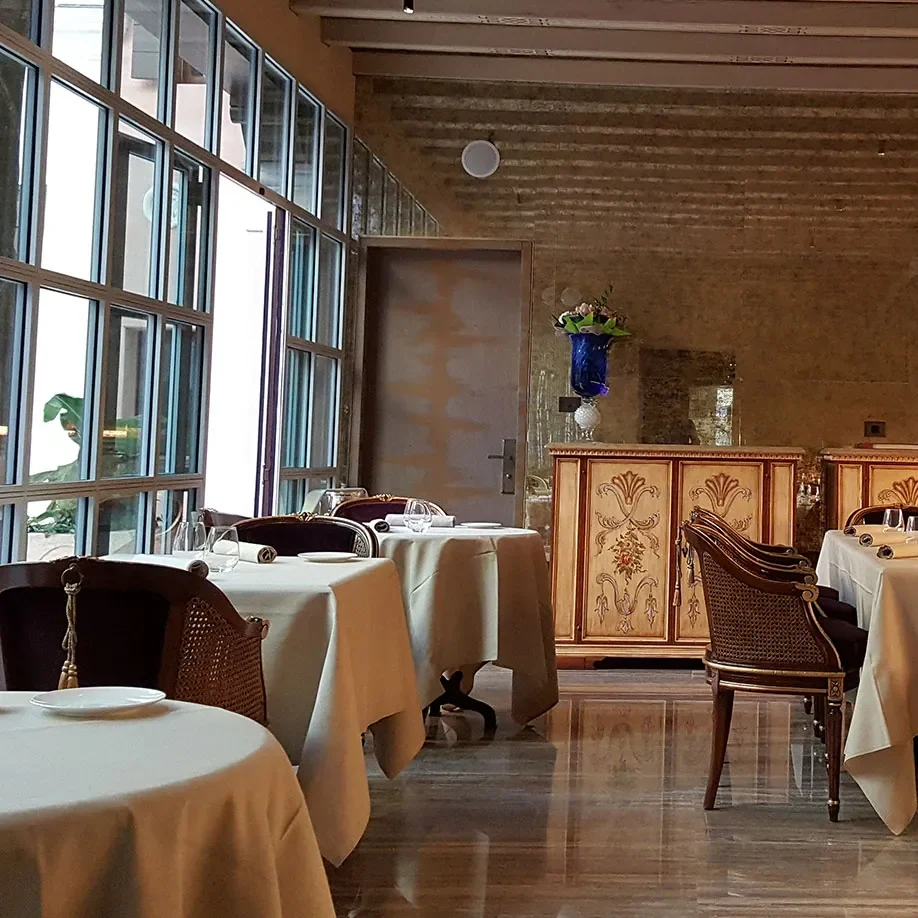 The old GLAM dining room, tables in cream linen under a beamed ceiling, painted credenzas along the end wall and framed prints down the right