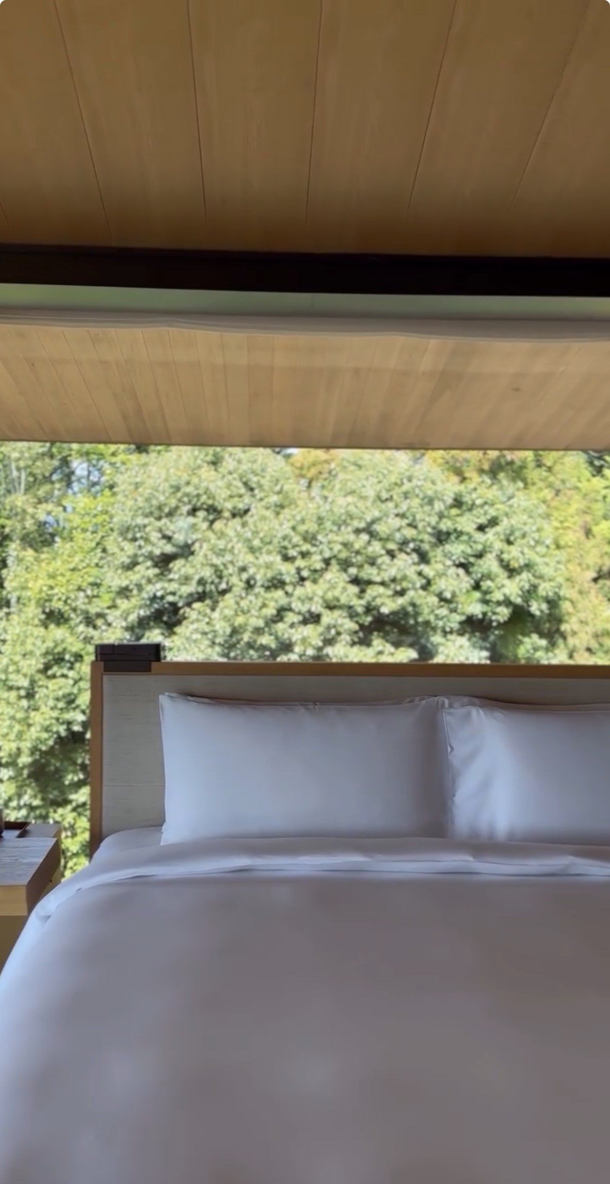 A bed made up in white with the garden through the window behind it