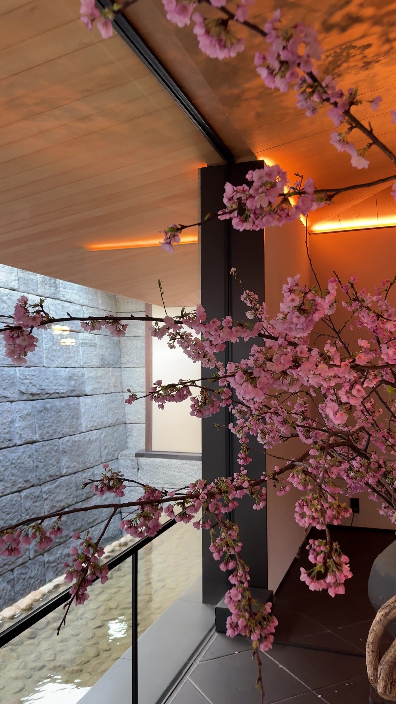 A branch of pink cherry blossom against a lit stone wall in the lobby
