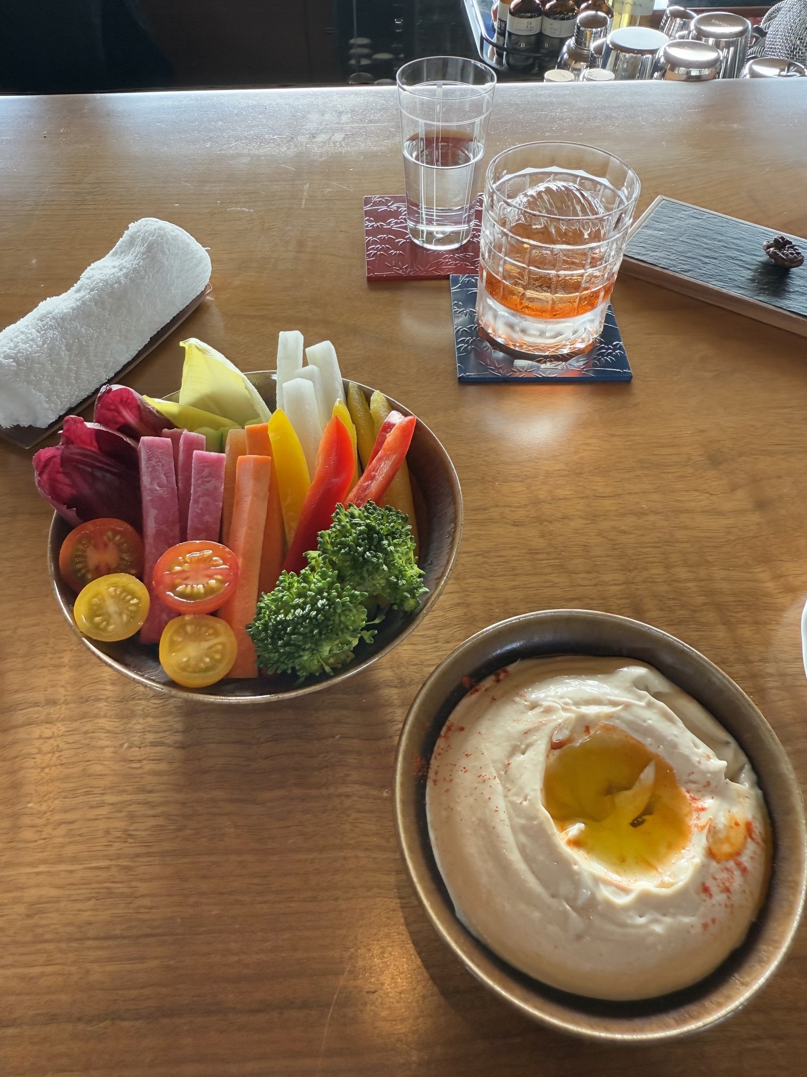 A bowl of raw vegetables and a dish of hummus with an egg yolk on a timber table