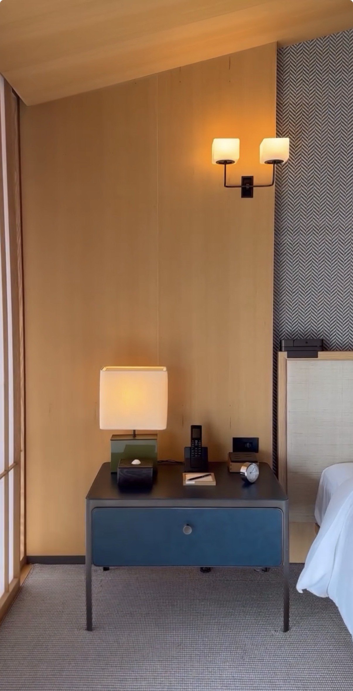A bedside table with a lamp, a tray and a dark blue drawer unit beside the bed
