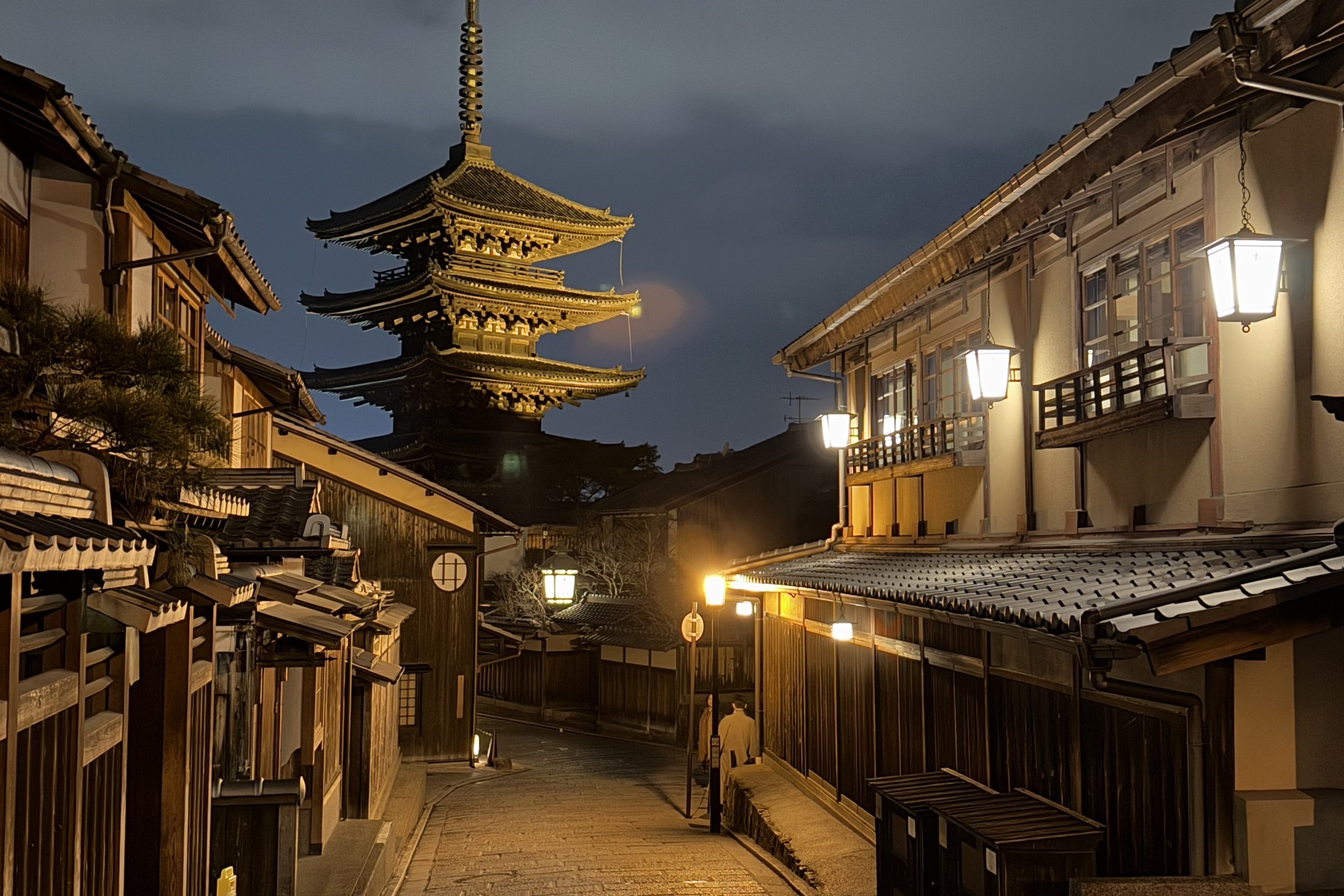 The lantern-lit lane of Ninenzaka at night with the Yasaka pagoda above the wooden houses