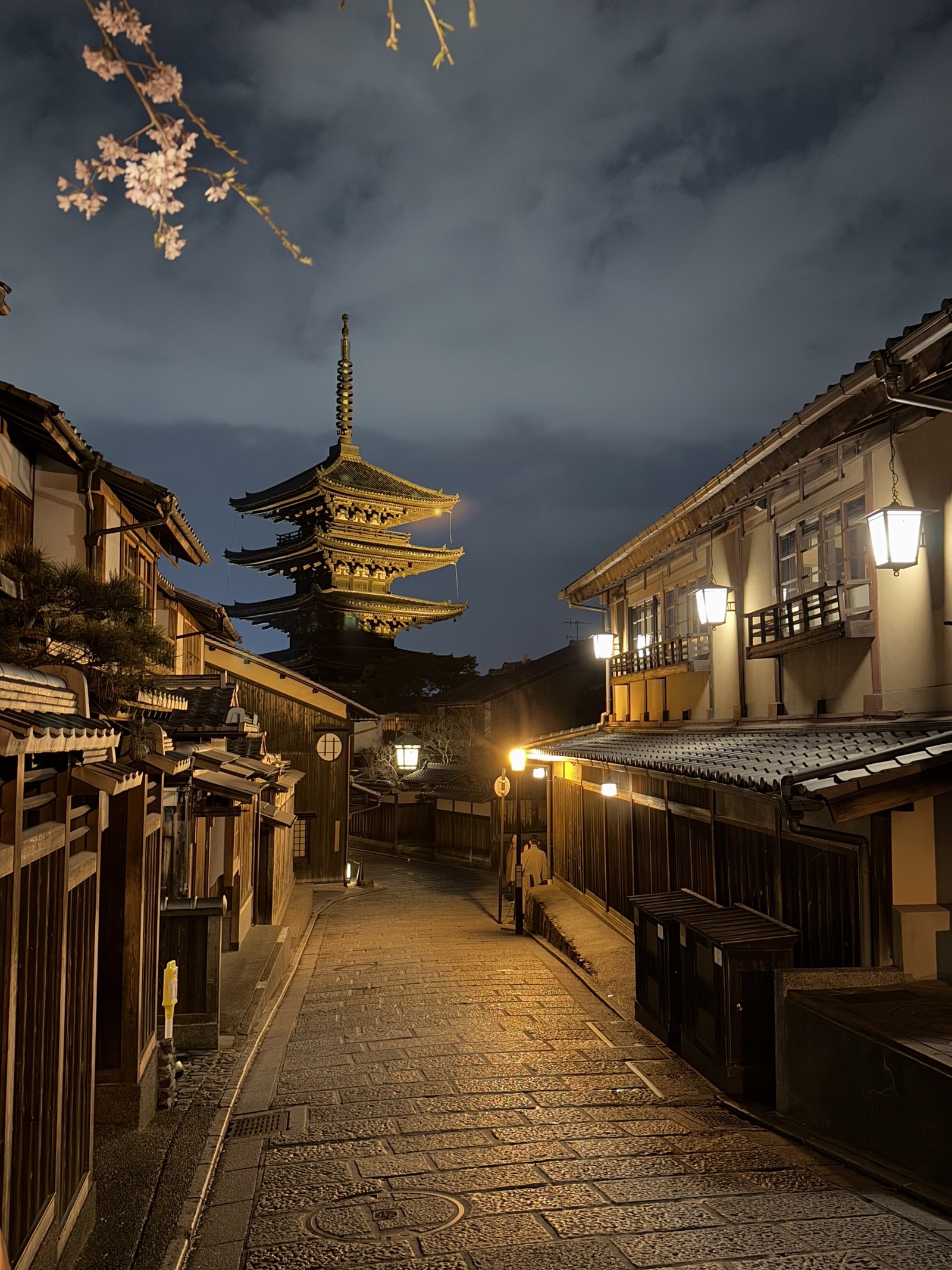 A stepped lane of timber houses lit by lanterns with the pagoda rising at the end