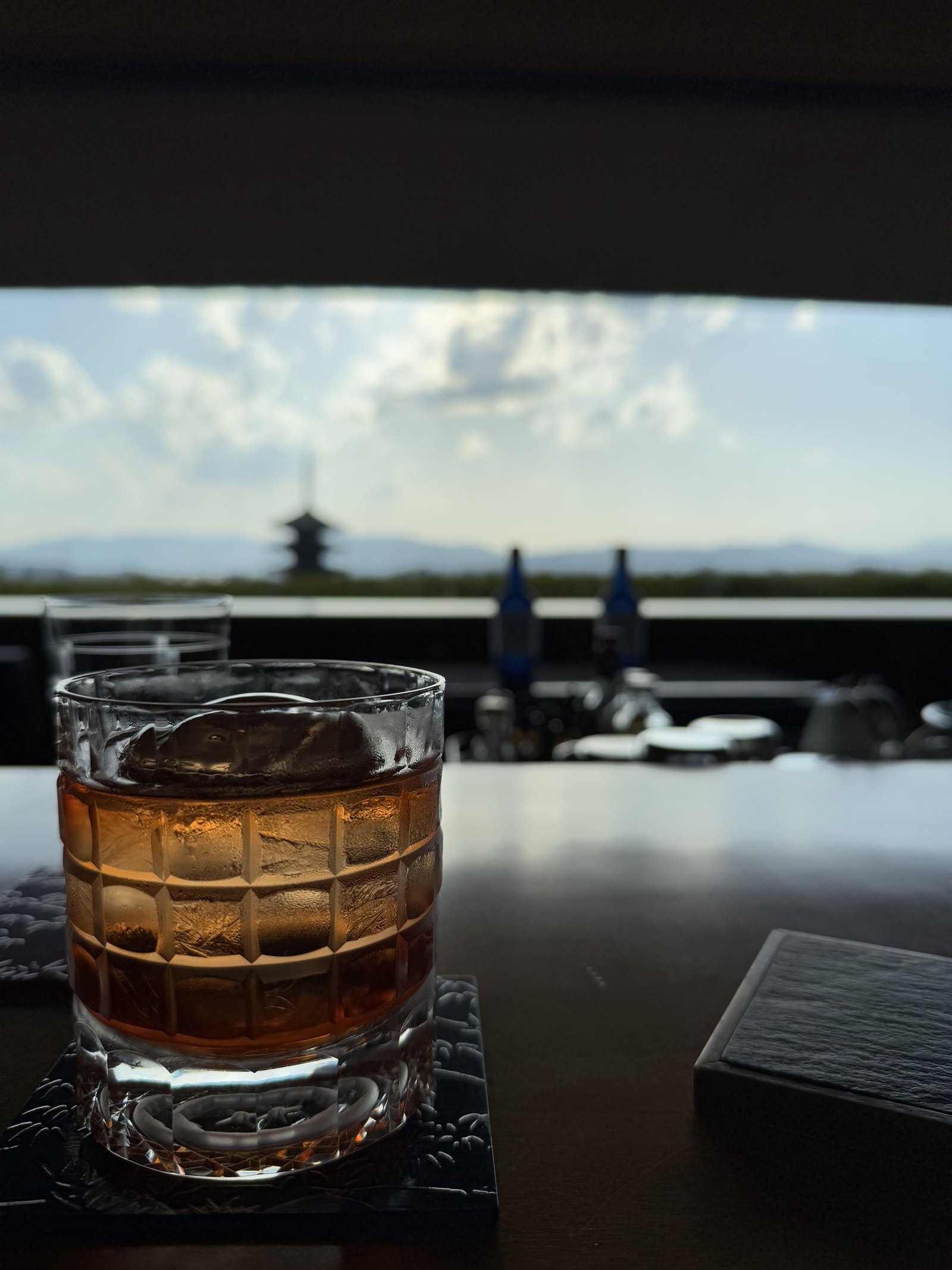 A cut glass of whisky on the bar with the pagoda and the hills beyond at sunset