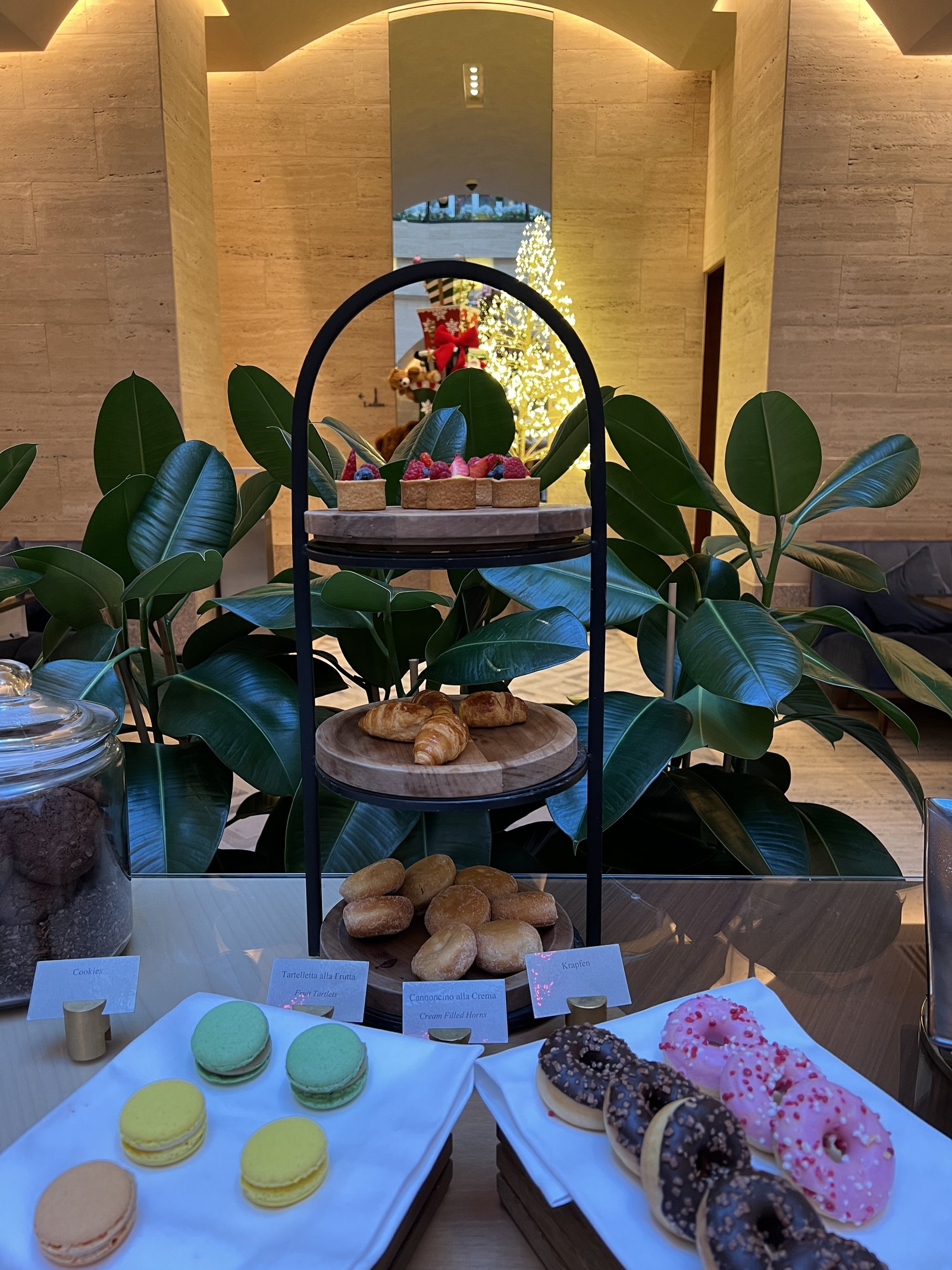 A three-tier stand with croissants, macarons and doughnuts on a table set with a plant